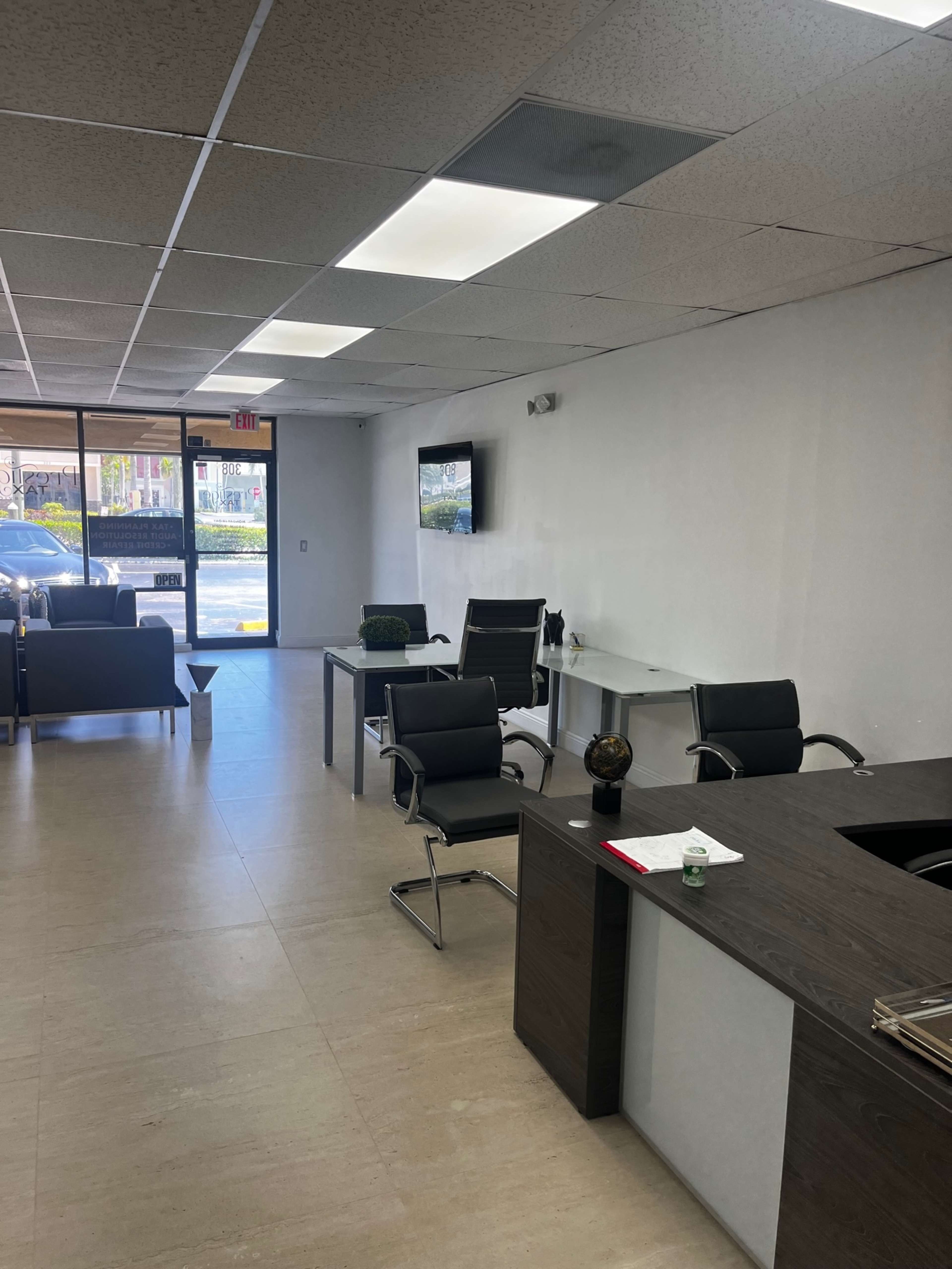 An office interior with a reception area featuring a desk, several chairs, and a television mounted on the wall.