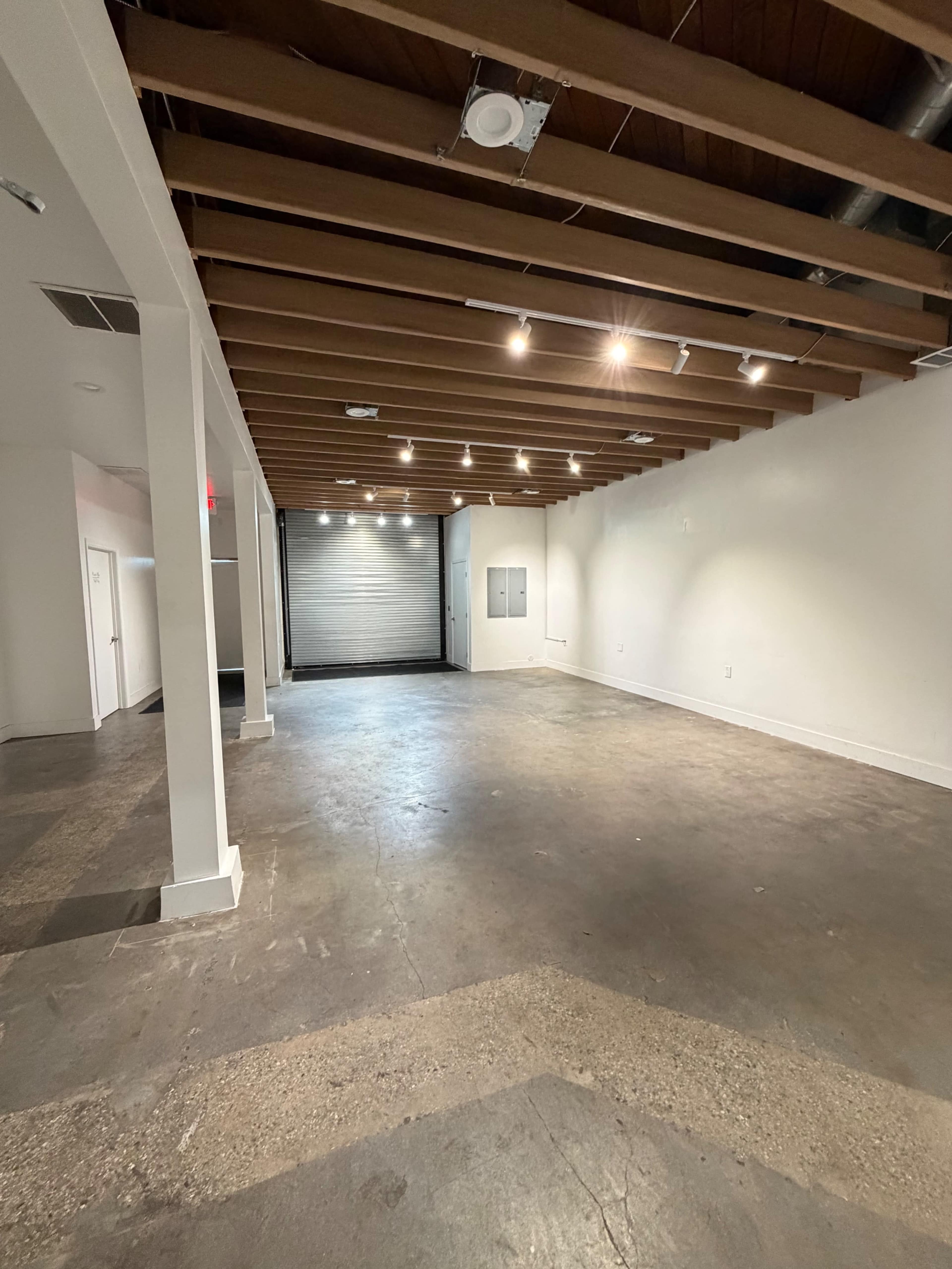 The image shows an empty room with exposed wooden beams on the ceiling and a concrete floor.
