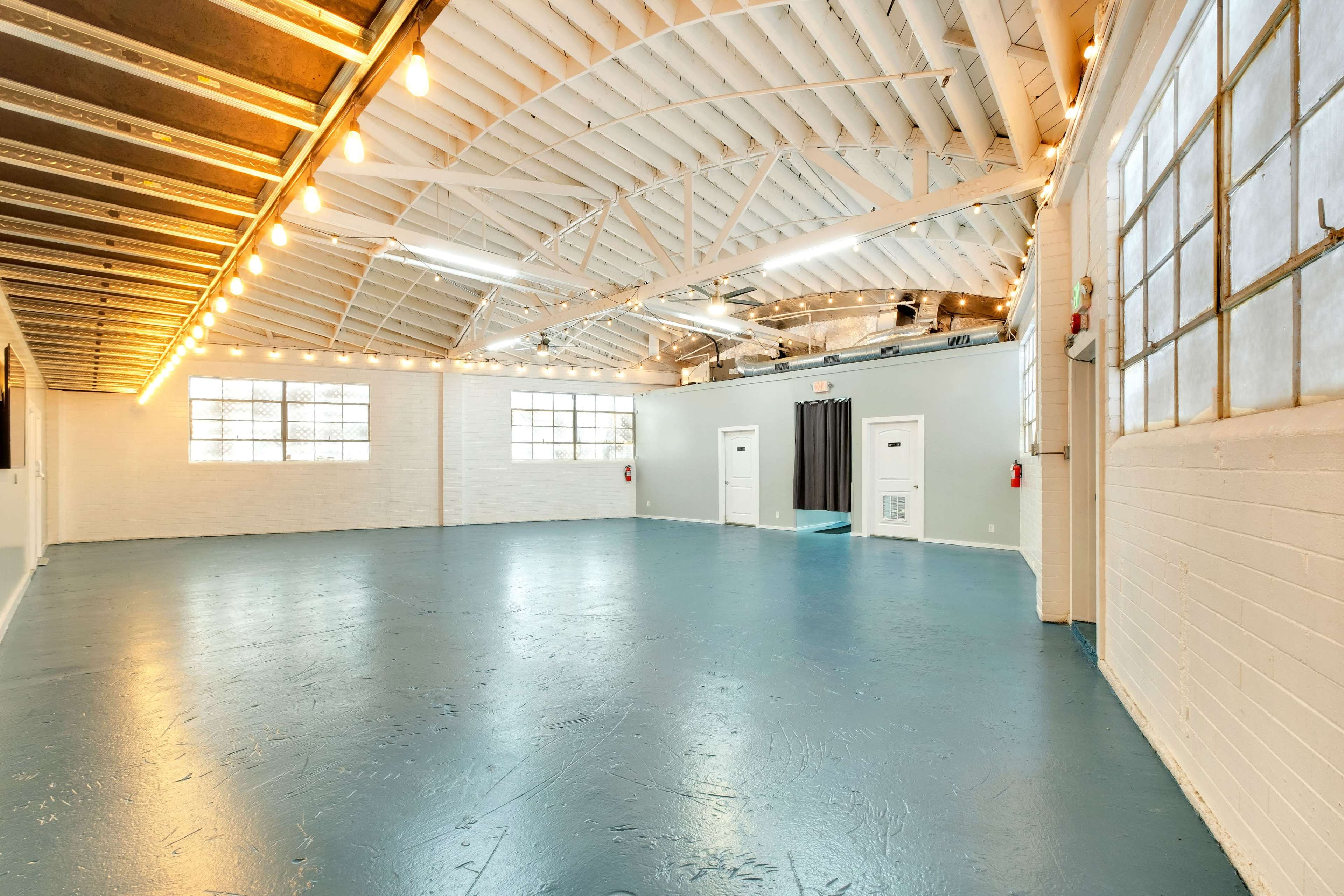 A spacious, brightly lit interior with a polished blue floor and exposed white beams overhead.