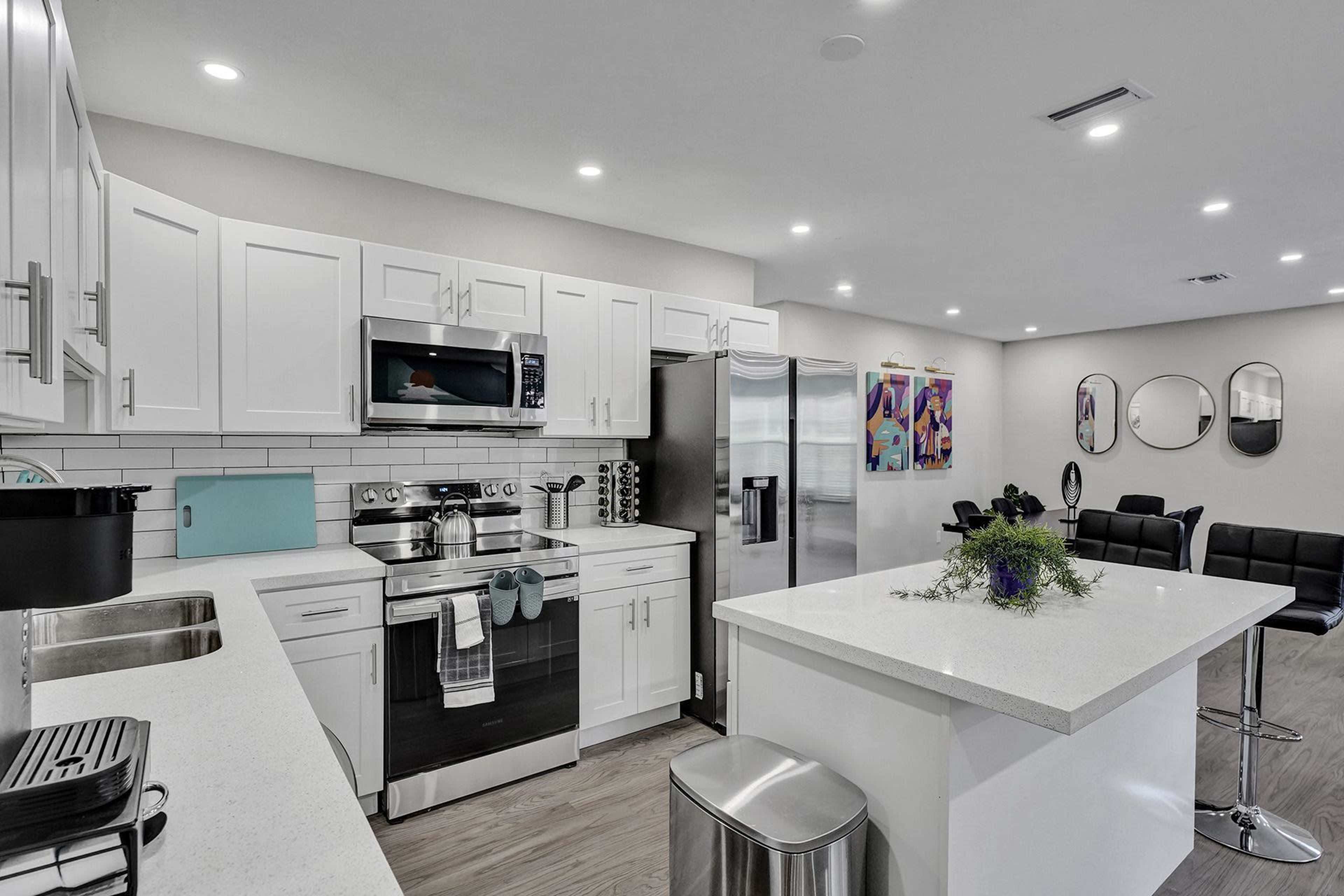 A modern kitchen features white cabinetry, stainless steel appliances, and a centralized island with a small floral arrangement.