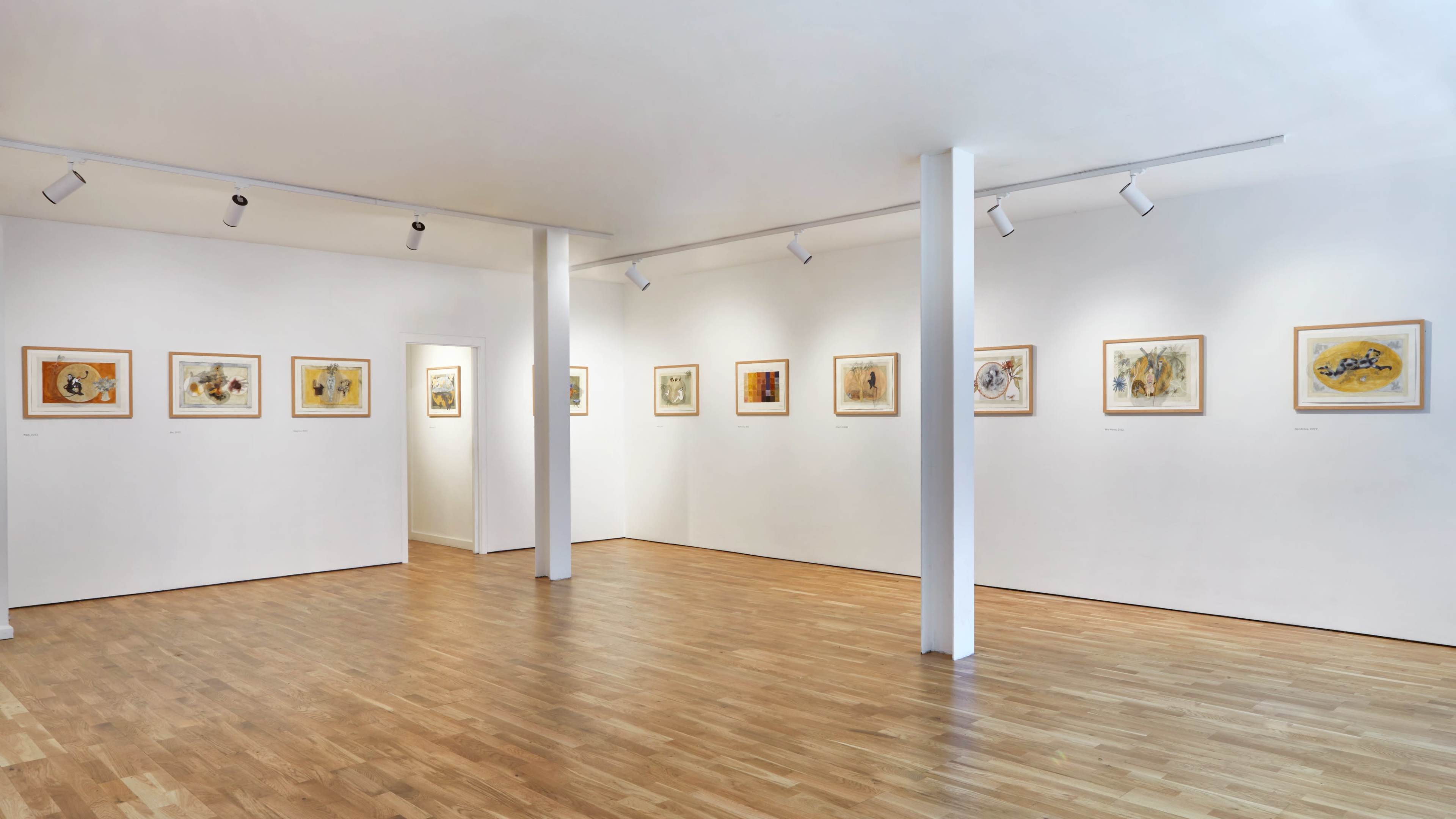 An art gallery with wooden flooring, displaying framed artworks on white walls.