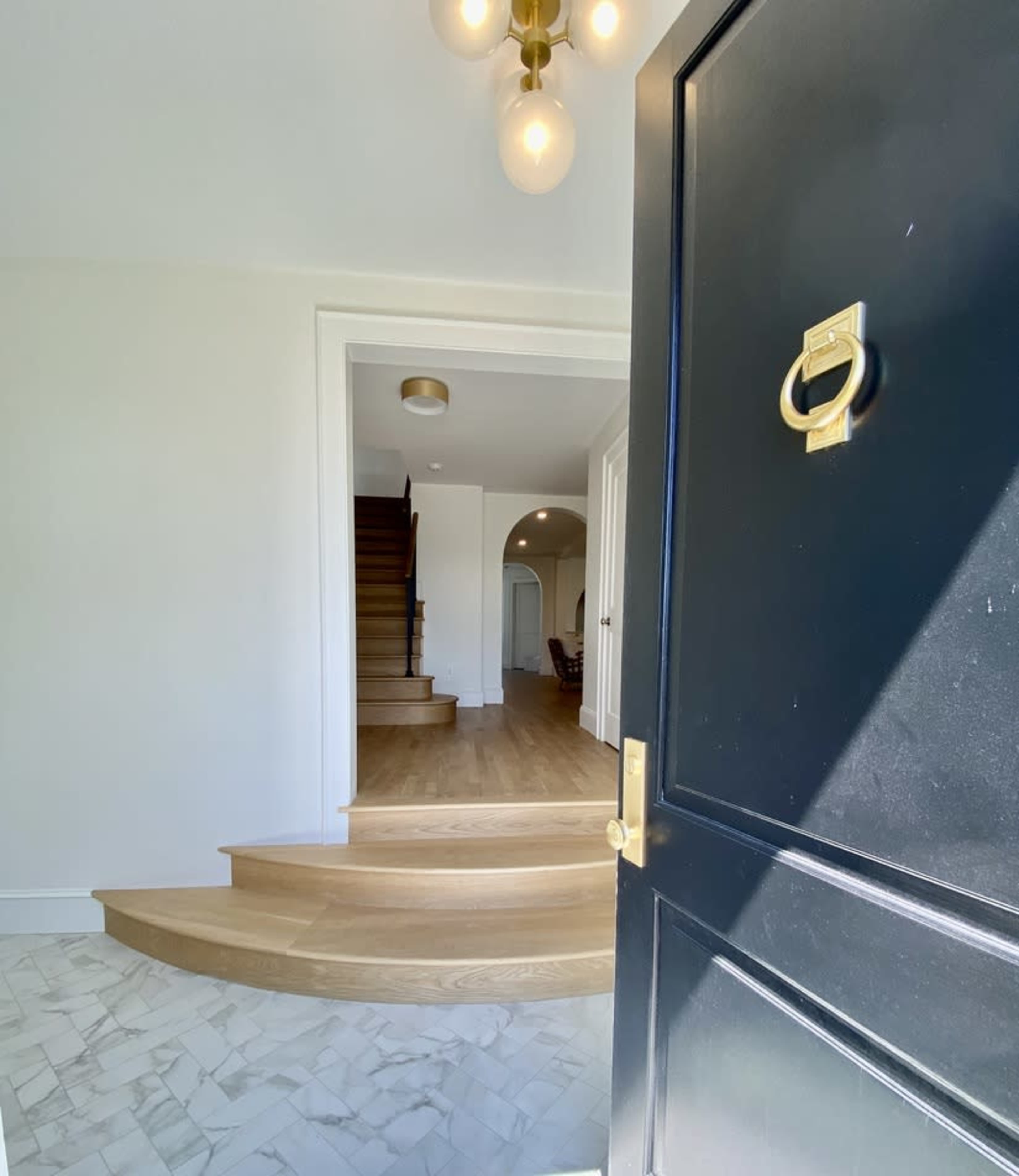 A black front door opens to reveal a spacious entryway with curved wooden stairs leading to the upper floor.