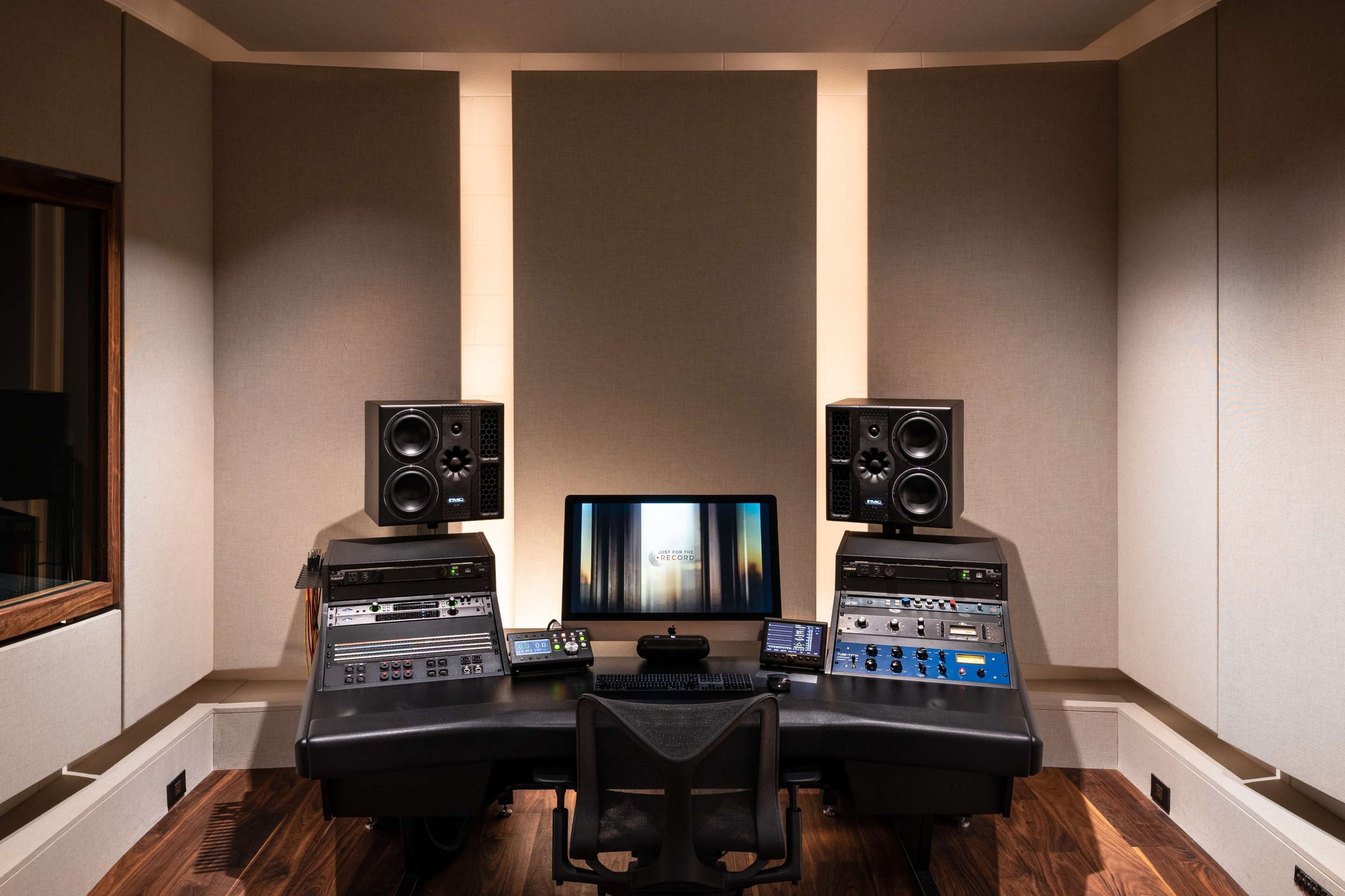 The image shows a modern audio mixing studio with a central workstation, multiple speakers, and a computer monitor displaying sound editing software.