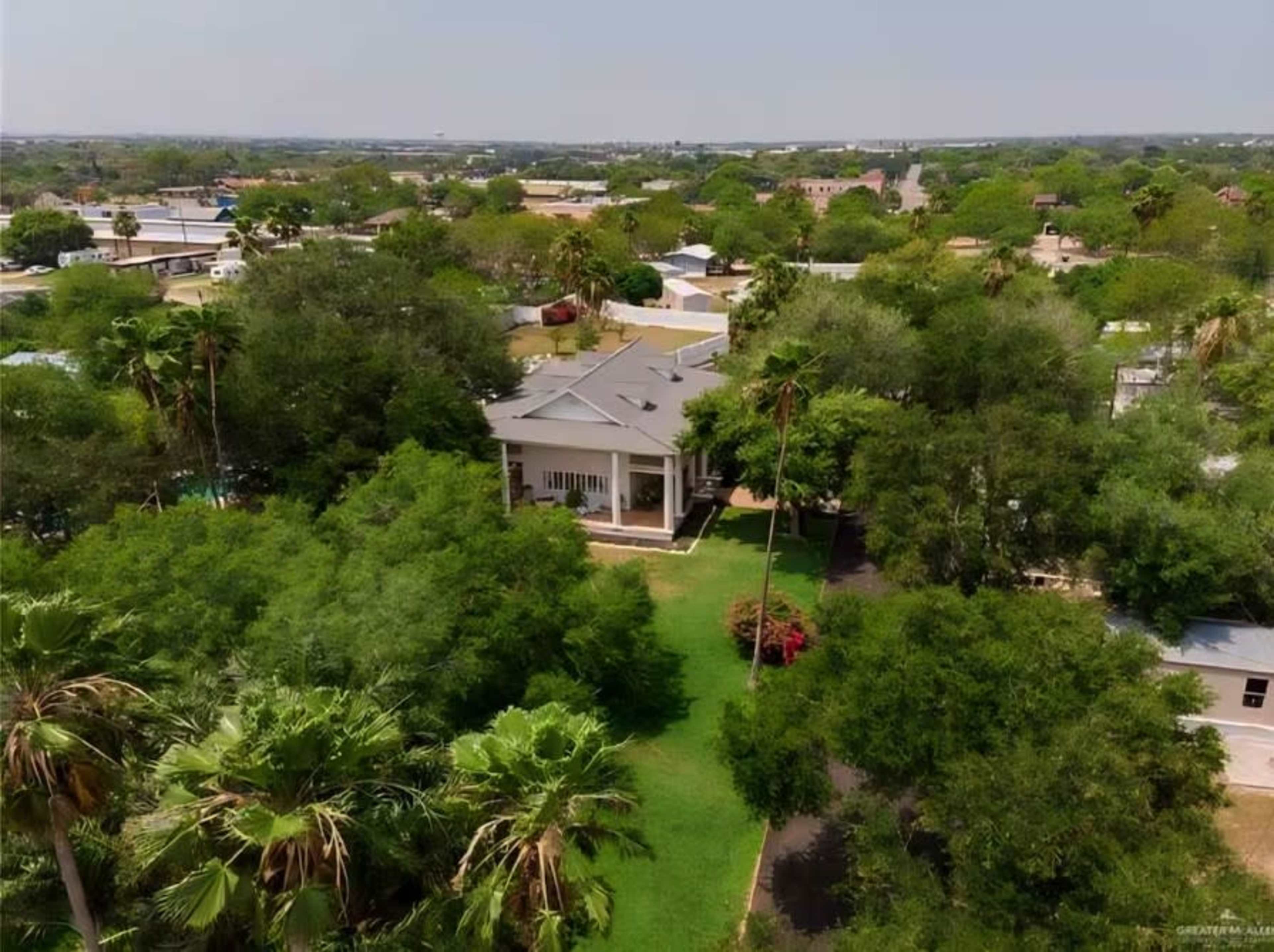 The image shows a large house surrounded by trees and greenery within a suburban area.