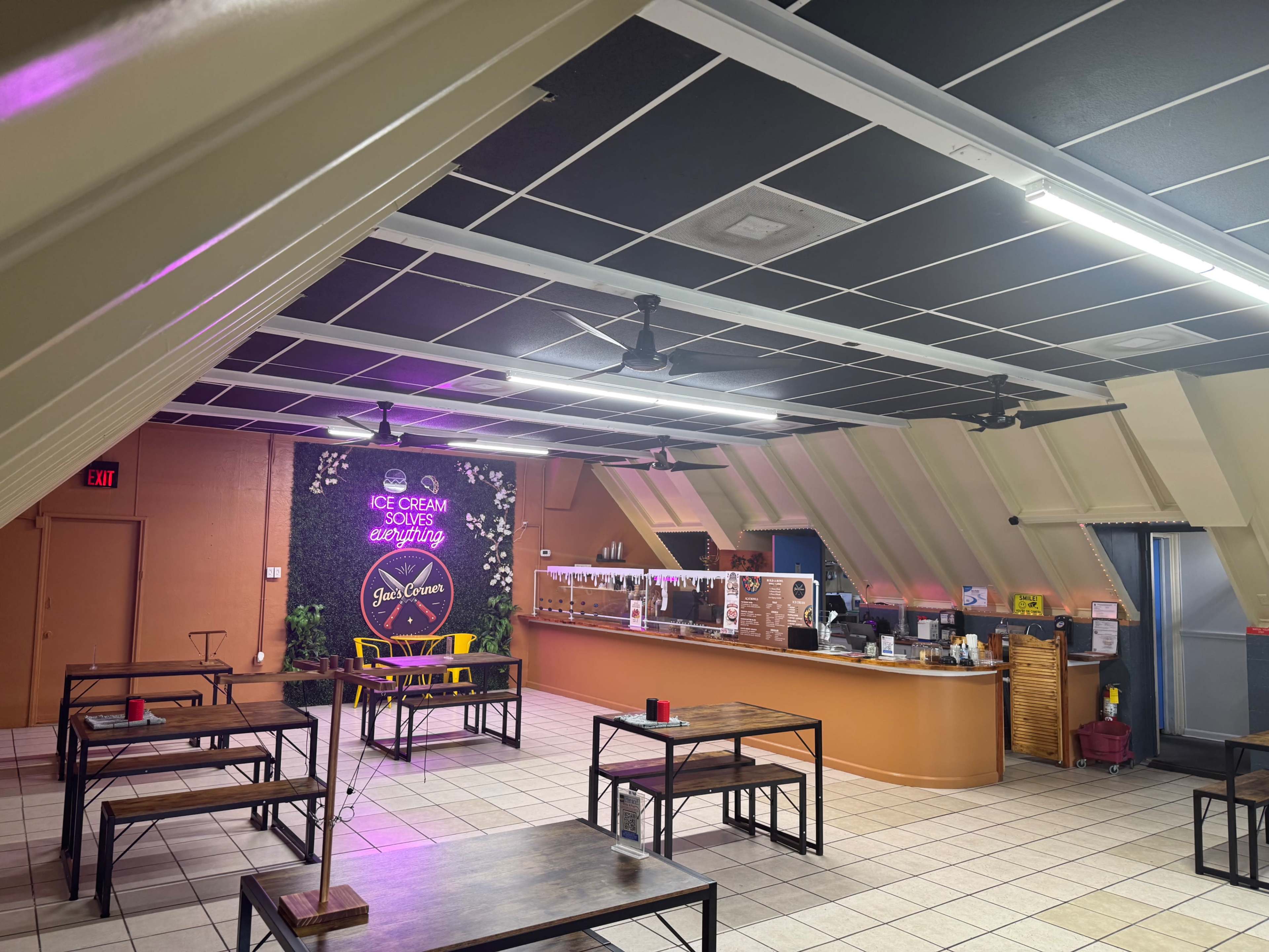 The image shows an ice cream shop interior with tables and a service counter featuring a floral backdrop and various ice cream toppings.