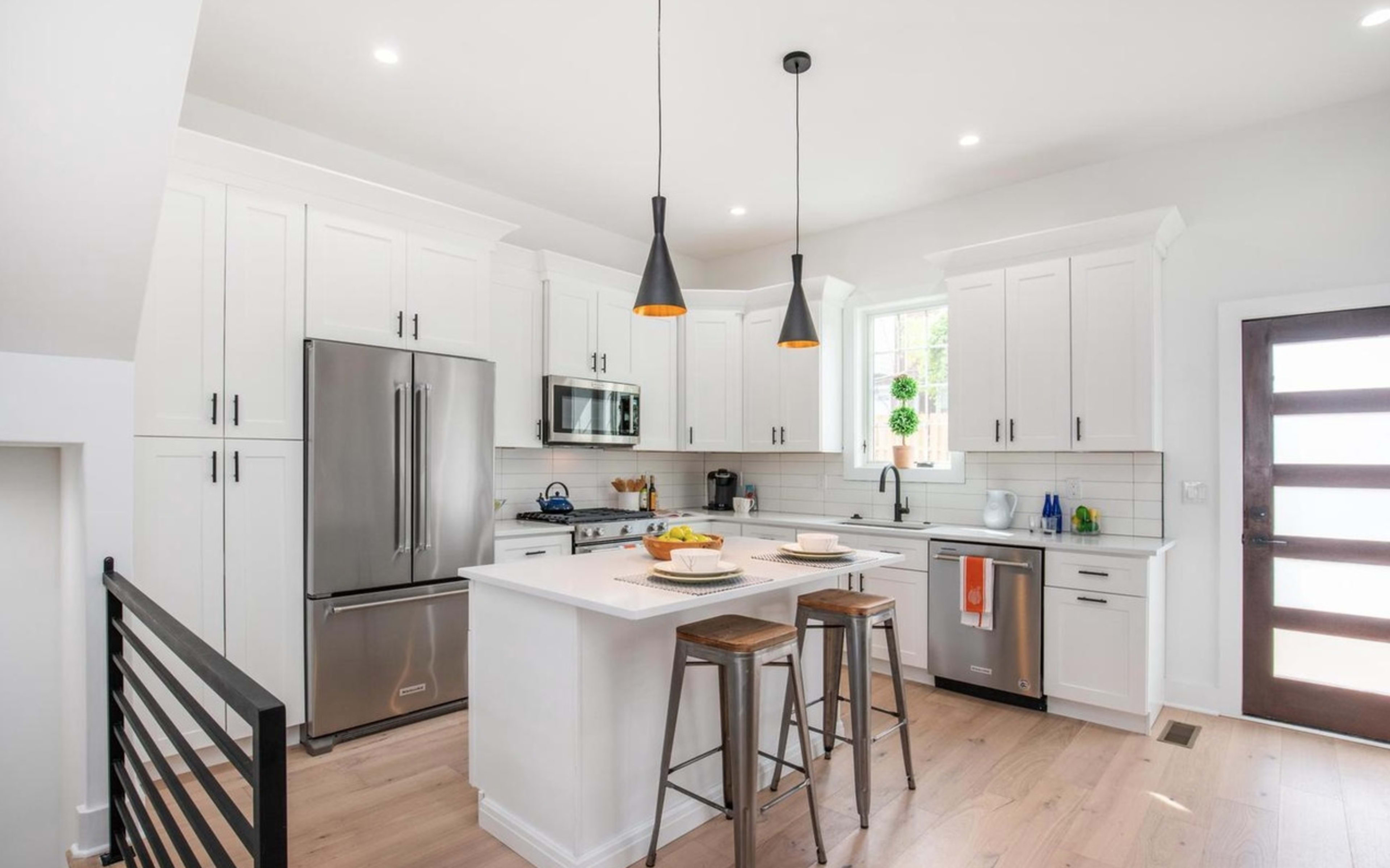 A modern kitchen features white cabinetry, stainless steel appliances, and a central island with bar stools.