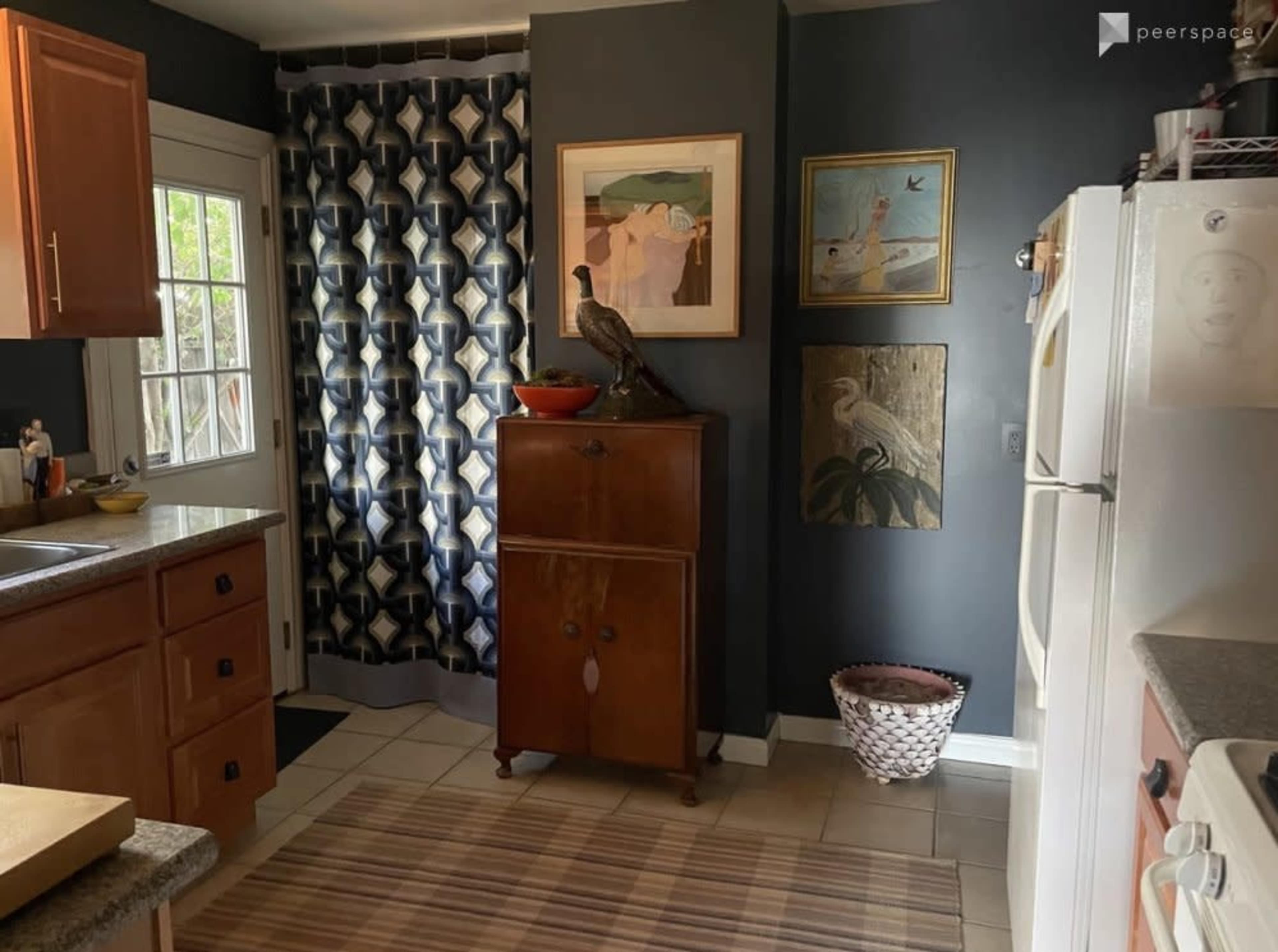 The image shows a kitchen with wooden cabinets, a decorative curtain, a vintage cabinet, and various wall art.