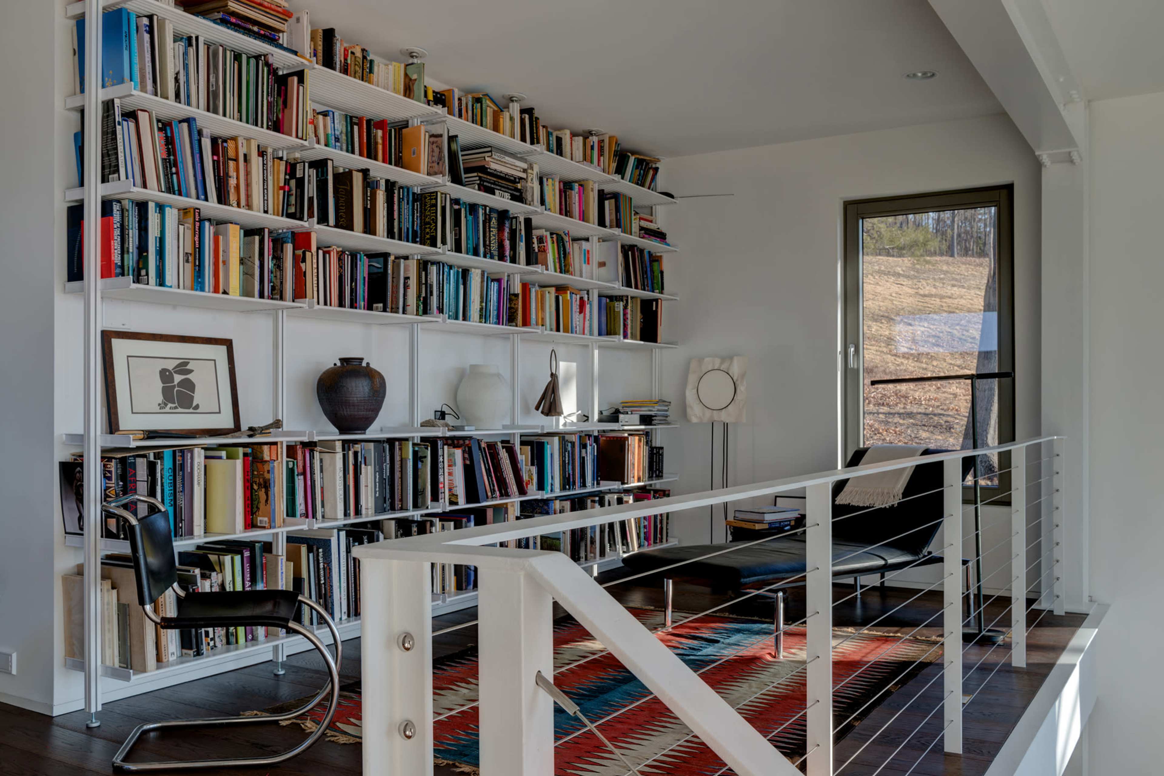 A modern library with floor-to-ceiling bookshelves filled with books, a black chair, and a colorful rug.