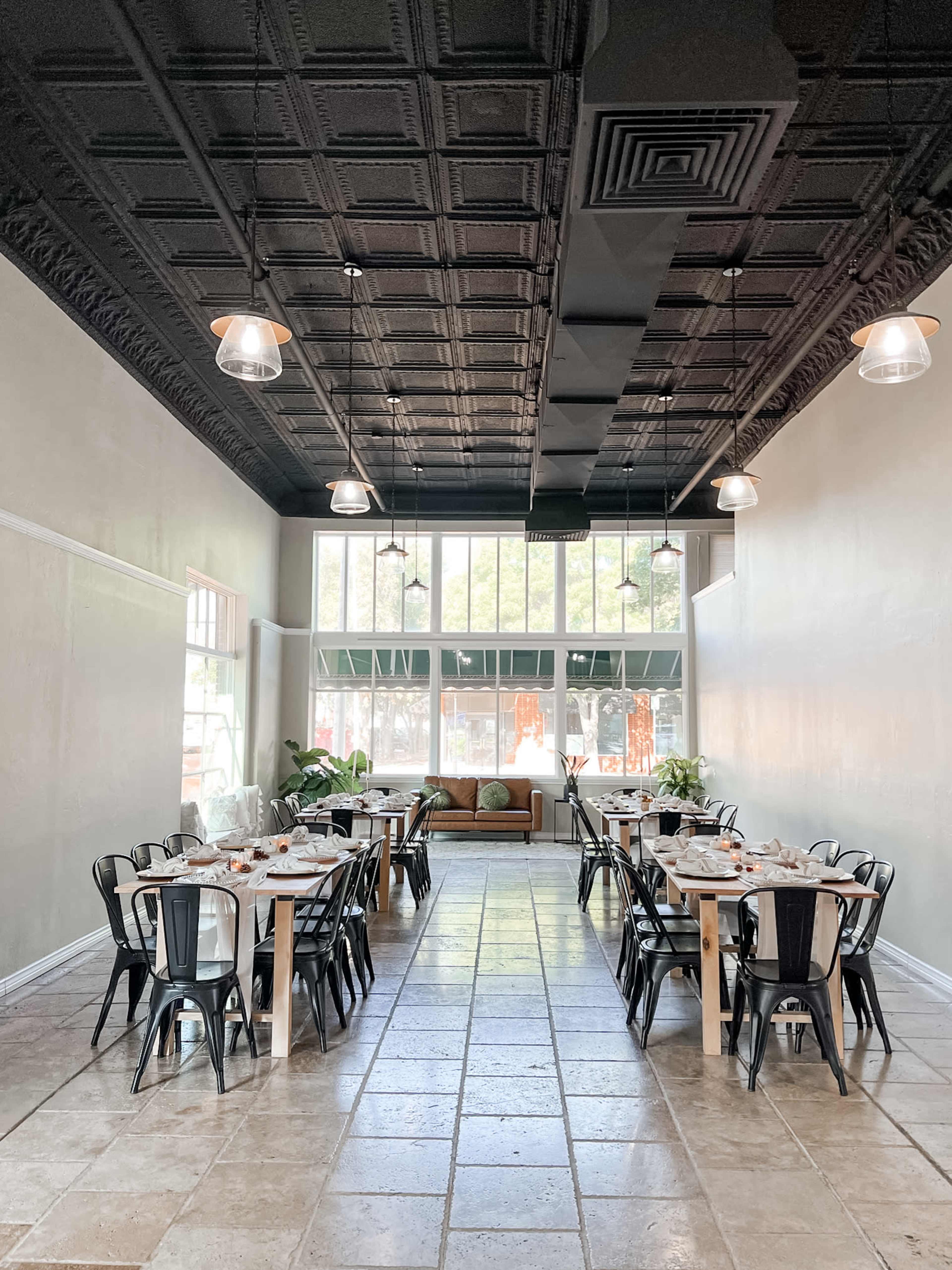 A spacious dining area with tables set for meals, black chairs, and large windows allowing natural light to enter.