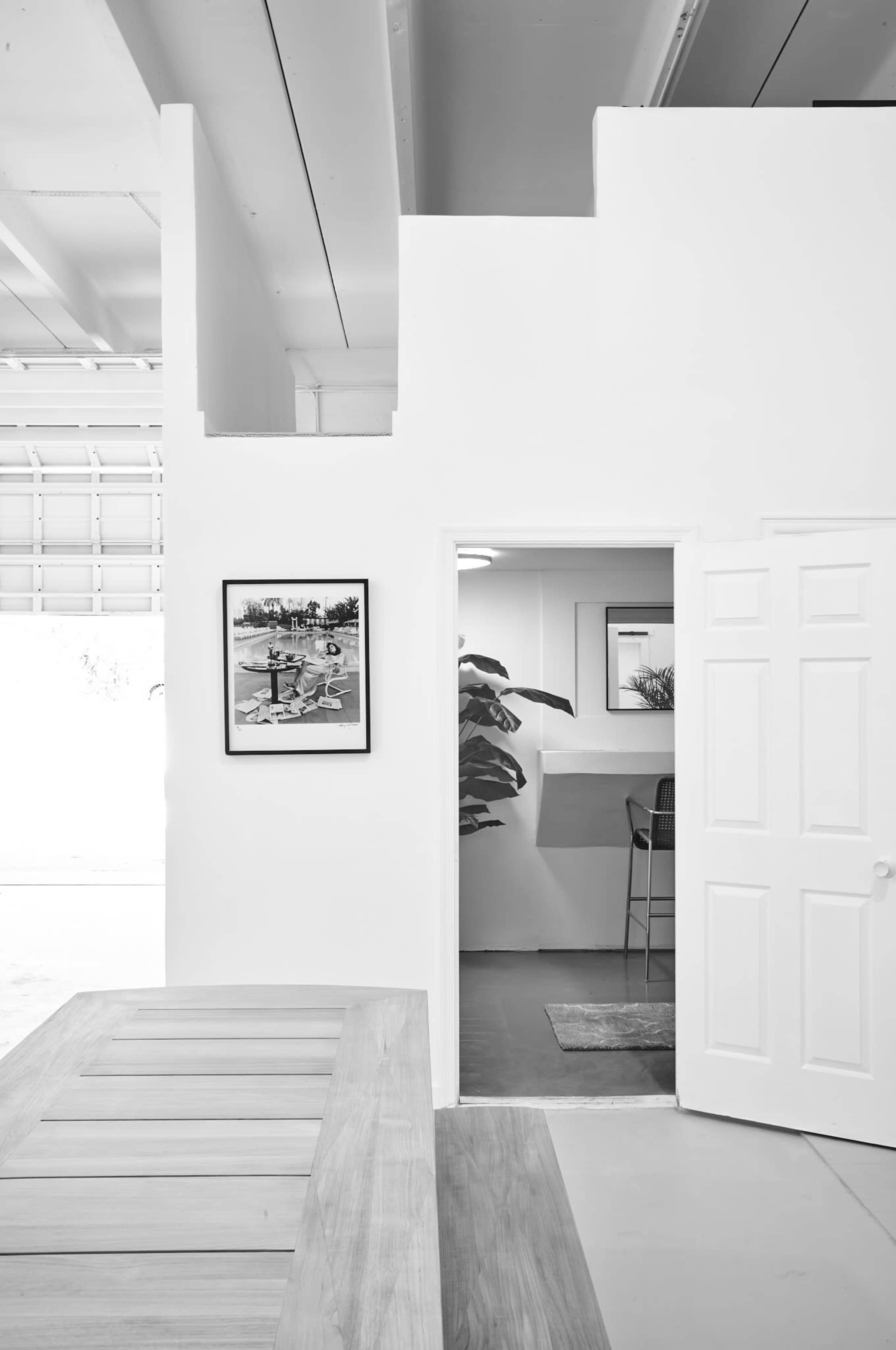 A minimalist interior space with white walls, a doorway leading into another room, and a framed photograph hanging on the wall.