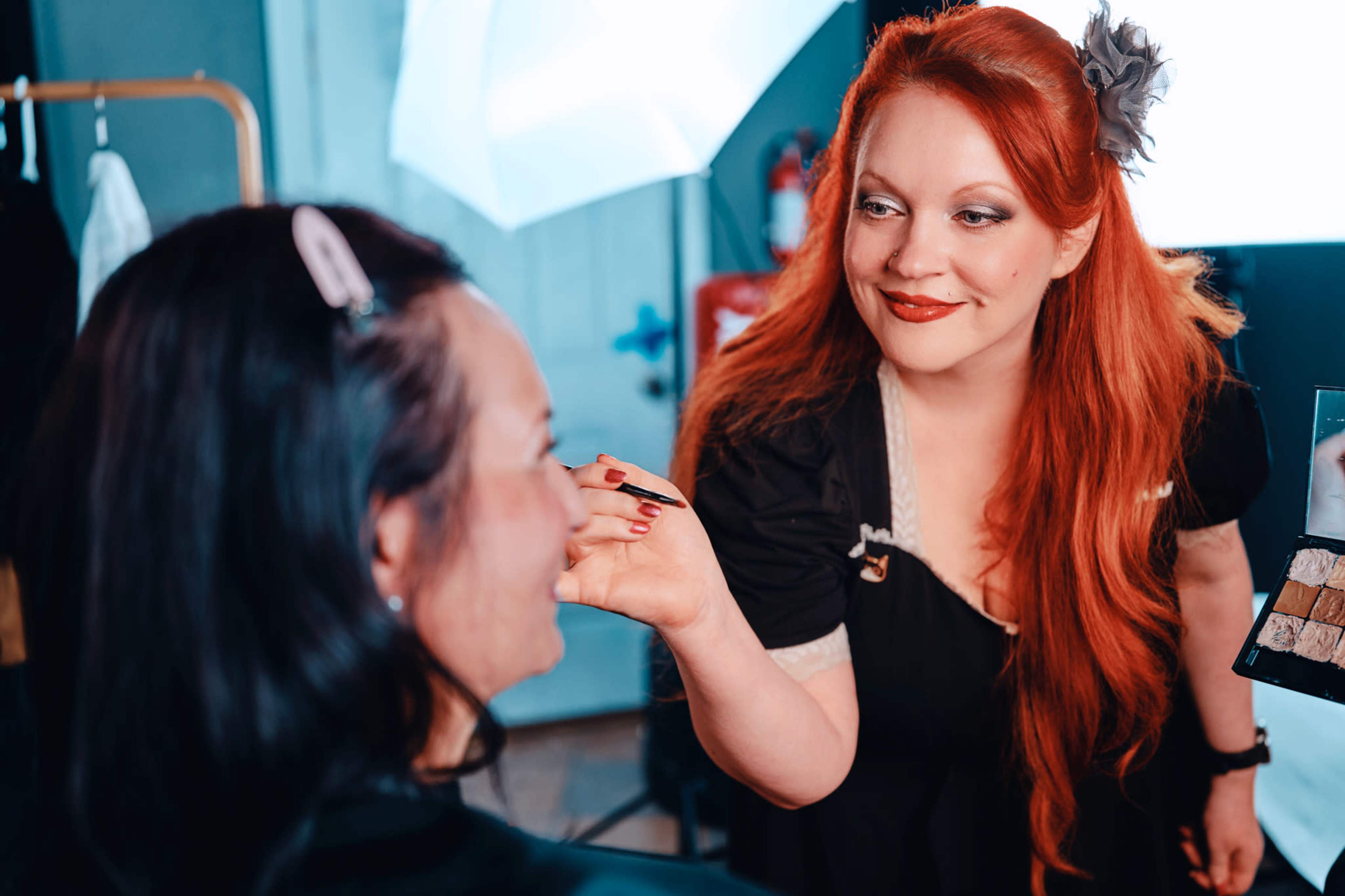 A makeup artist applies makeup to a client in a well-lit studio setting.