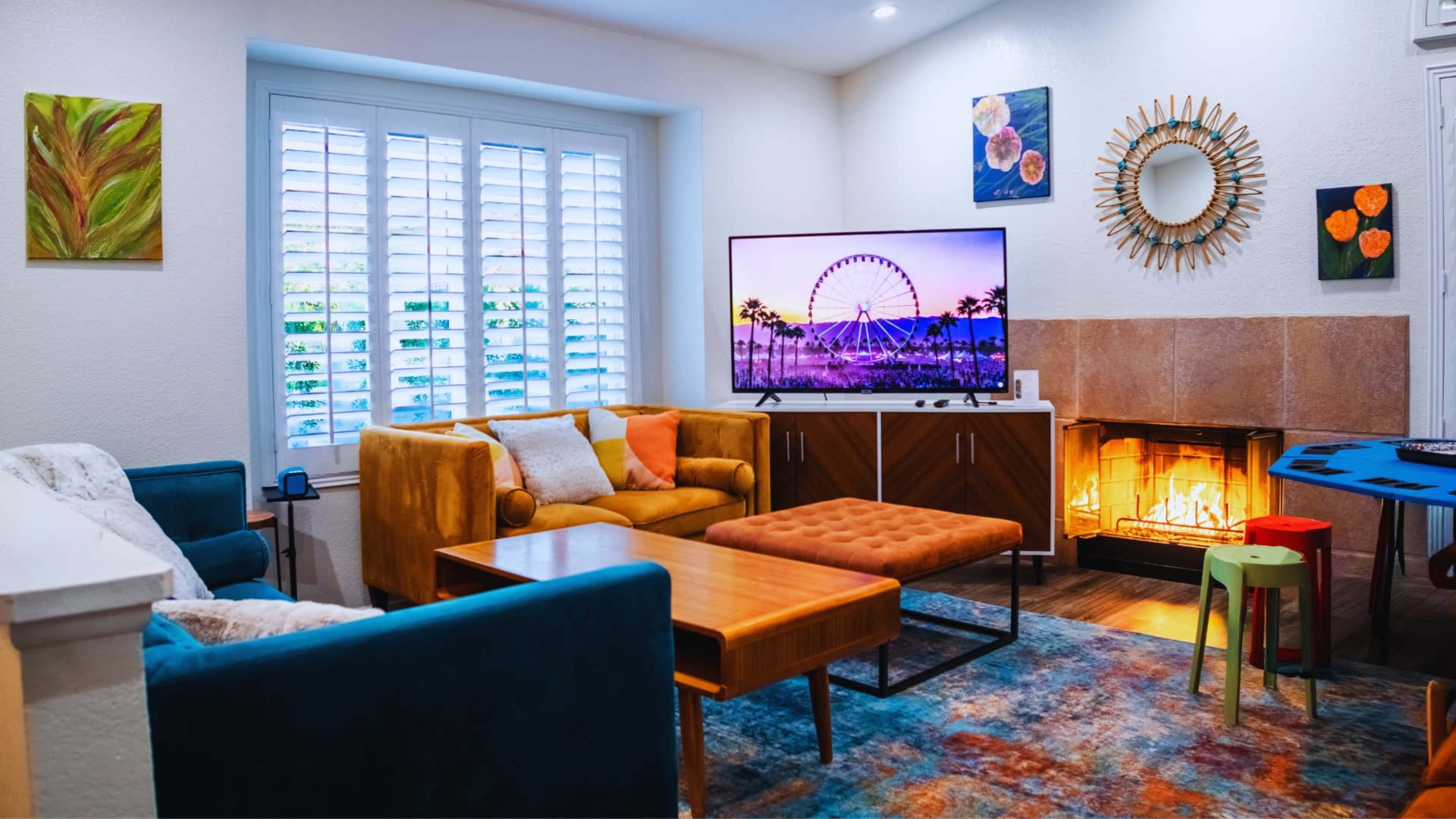 A cozy living room features a colorful sofa, a wooden coffee table, and a mounted TV displaying a ferris wheel, with a fireplace beside it.