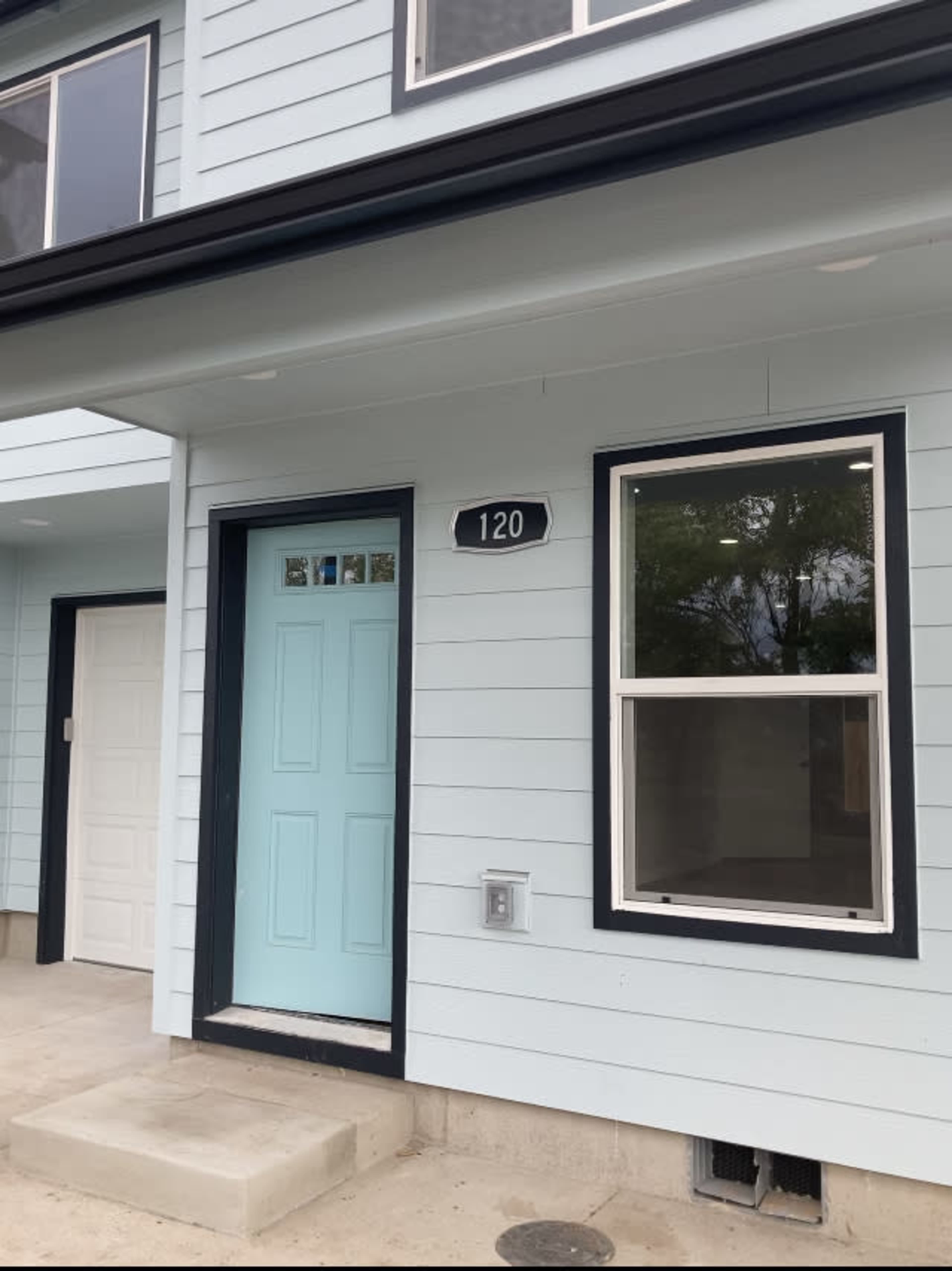 A modern light blue house exterior with a front door numbered 120 and a large window beside it.