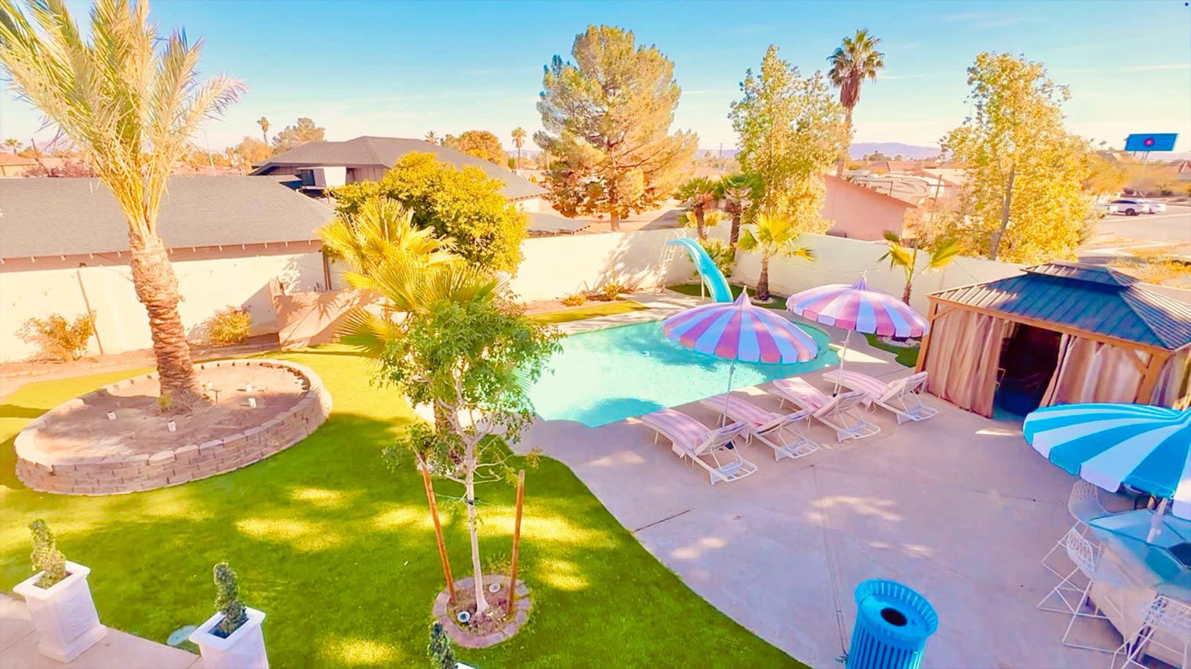 The image shows a residential backyard with a swimming pool, lounge chairs, palm trees, and several colorful umbrellas.