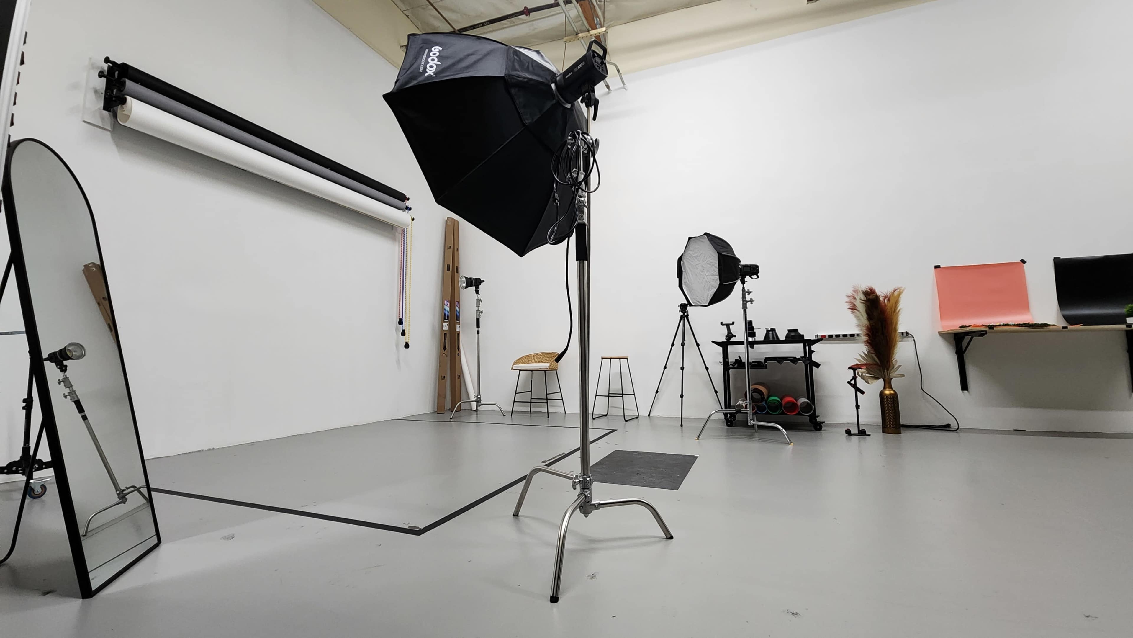 A photography studio equipped with lighting equipment, a large mirror, and various props arranged on the floor and shelves.