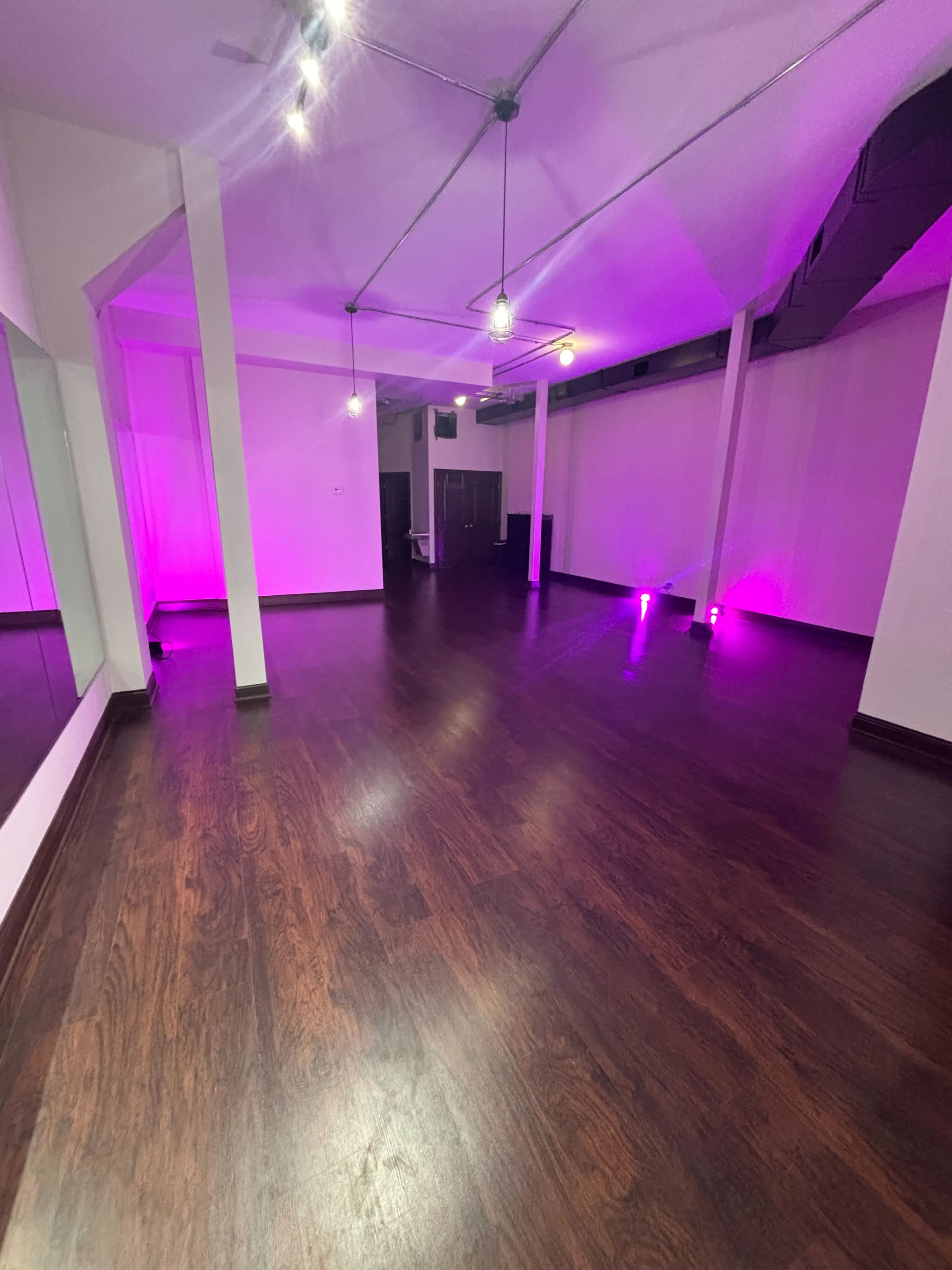 A spacious, well-lit room with dark wooden flooring and pink accent lighting.