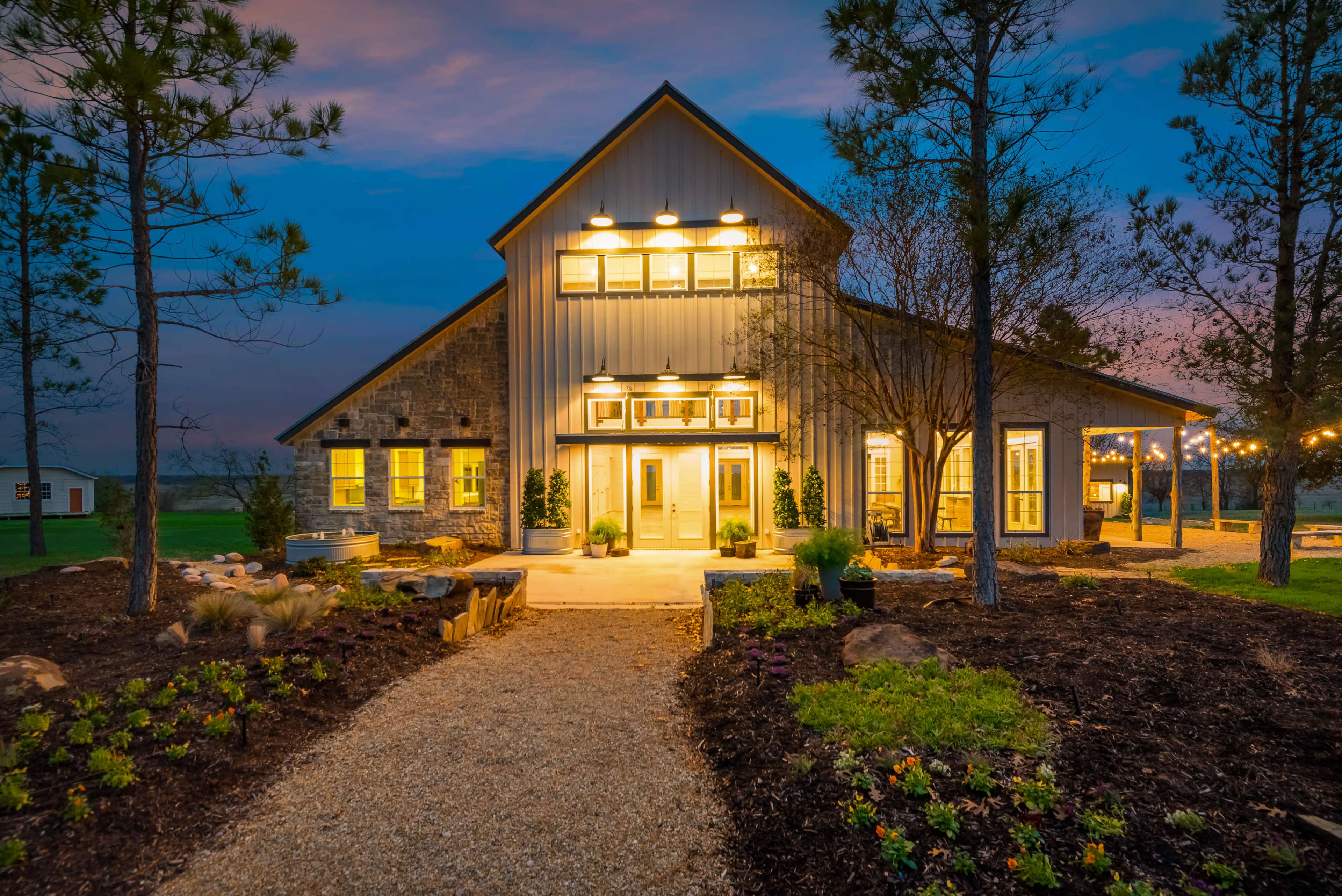 A modern two-story house with large windows is surrounded by neatly landscaped gardens and a gravel path leading to the entrance.