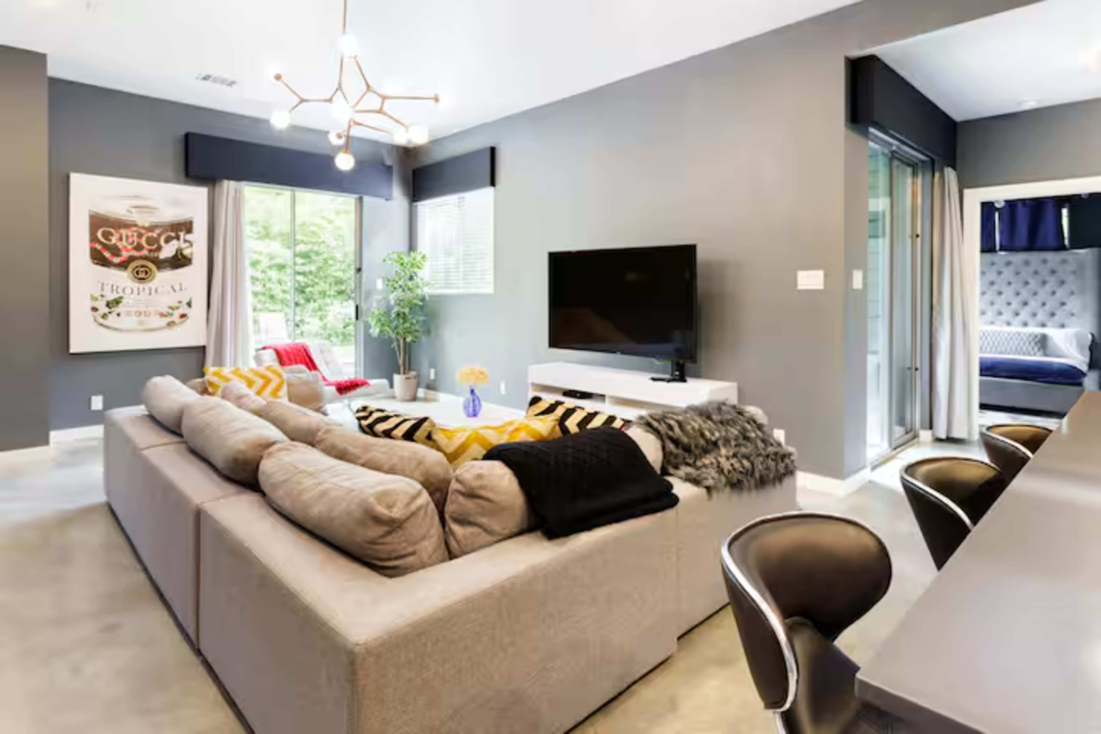 The image features a modern living room with a large sectional sofa, a television mounted on the wall, and a dining area in the background.