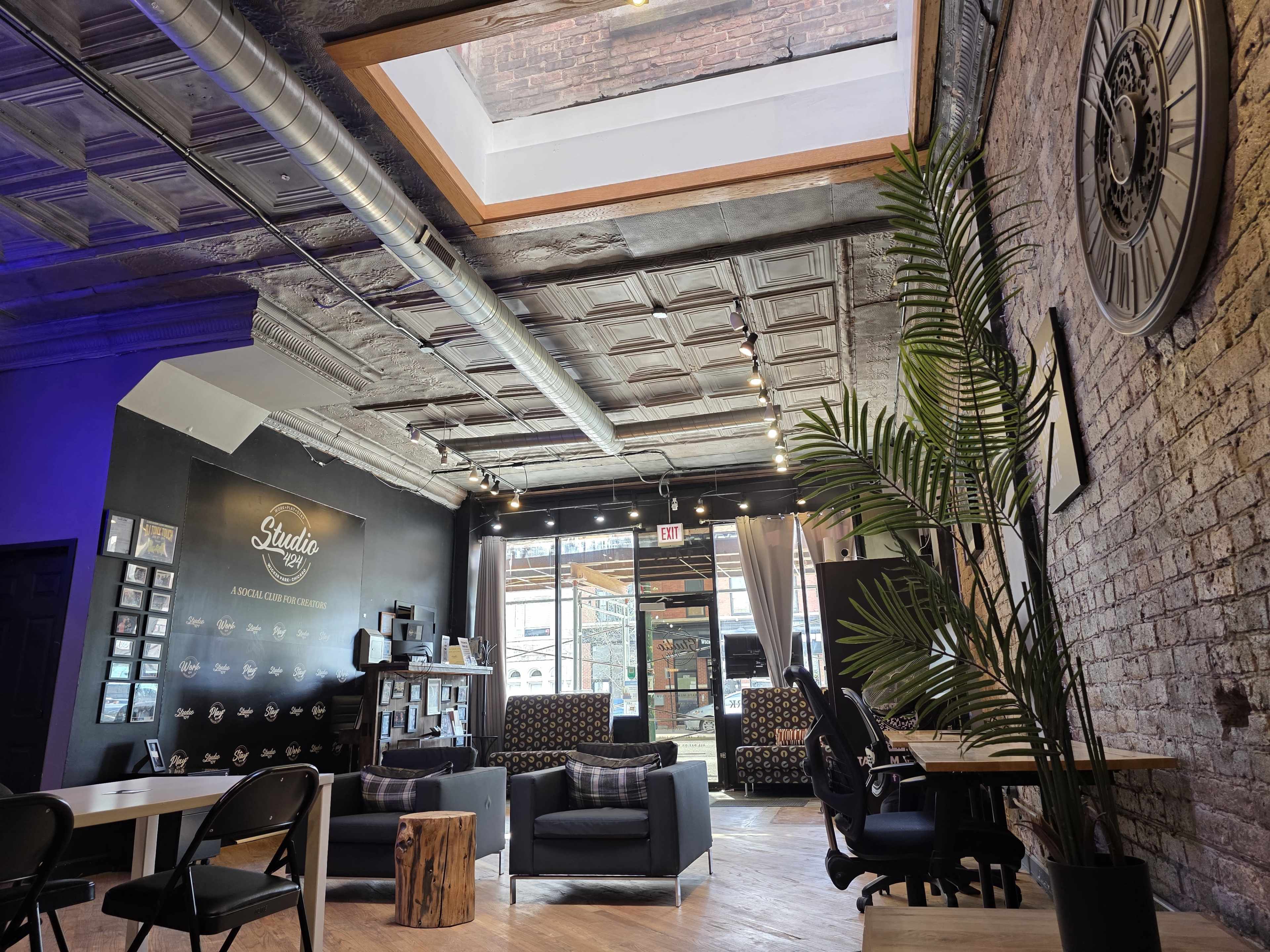 The image shows a contemporary interior of a studio with exposed brick walls, wooden flooring, and various seating arrangements, including modern chairs and couches.