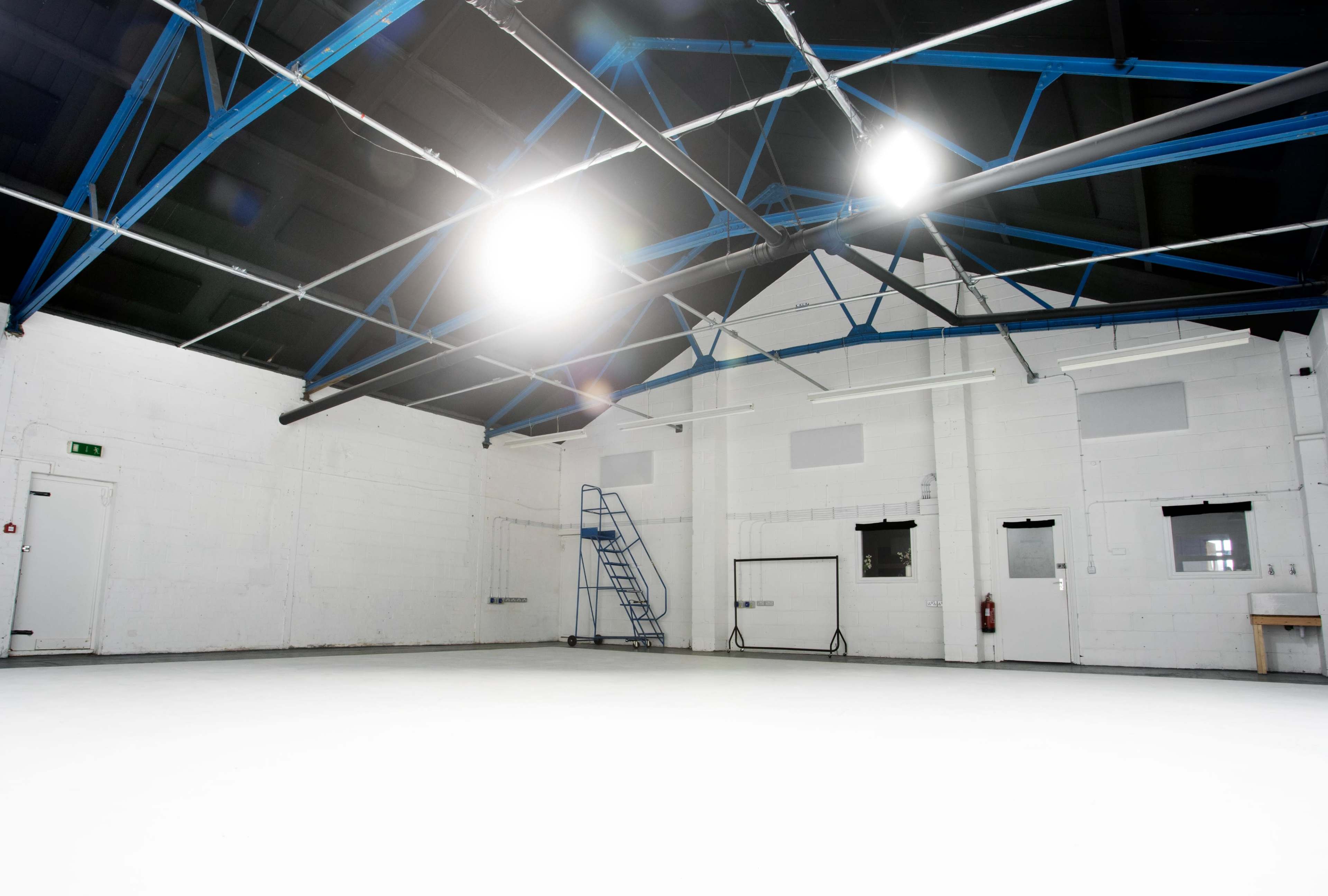 An empty industrial space with white walls, a smooth floor, and a blue metallic ceiling structure.