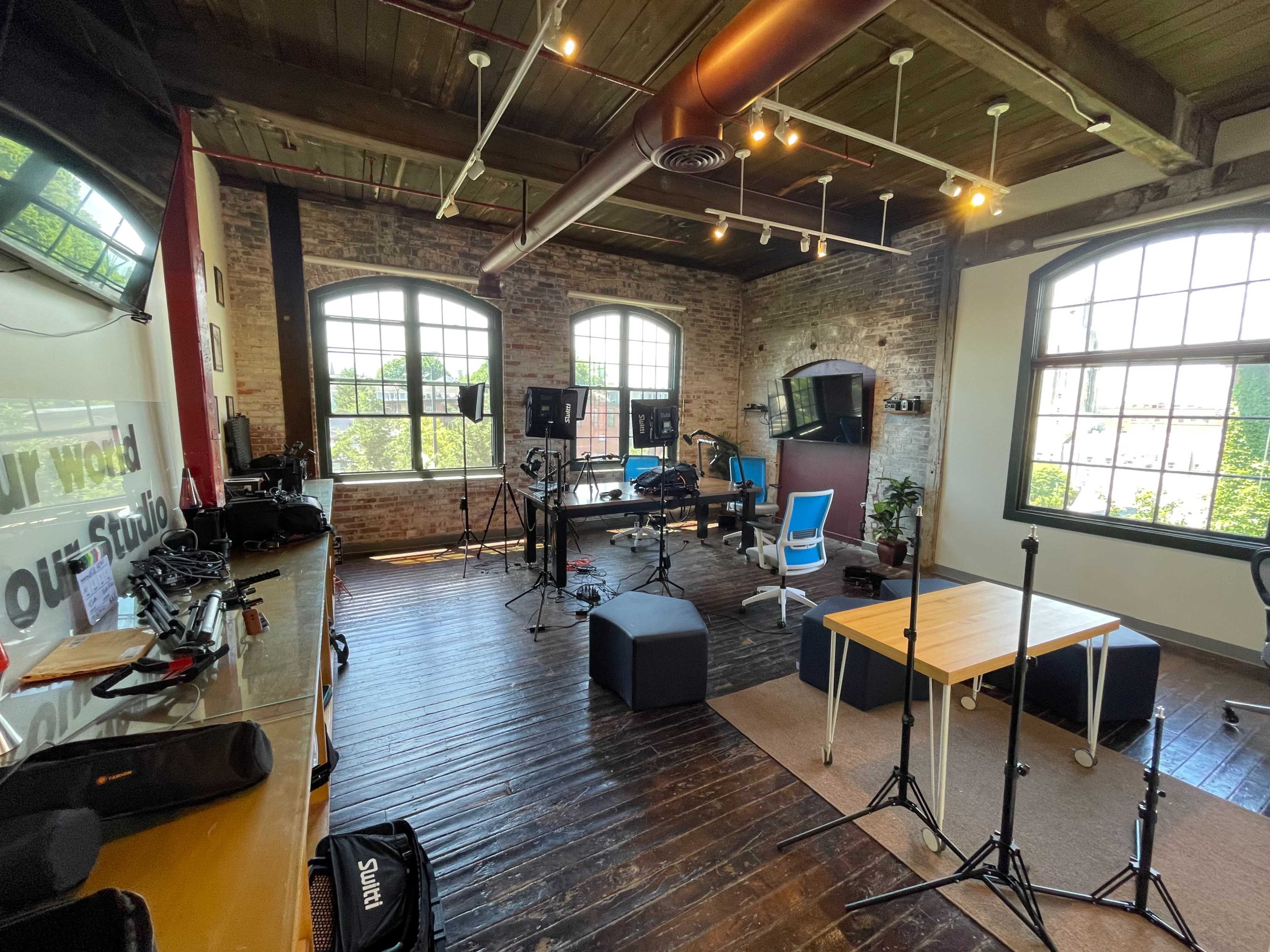 A spacious studio with wooden floors, large windows, and equipment set up for production.