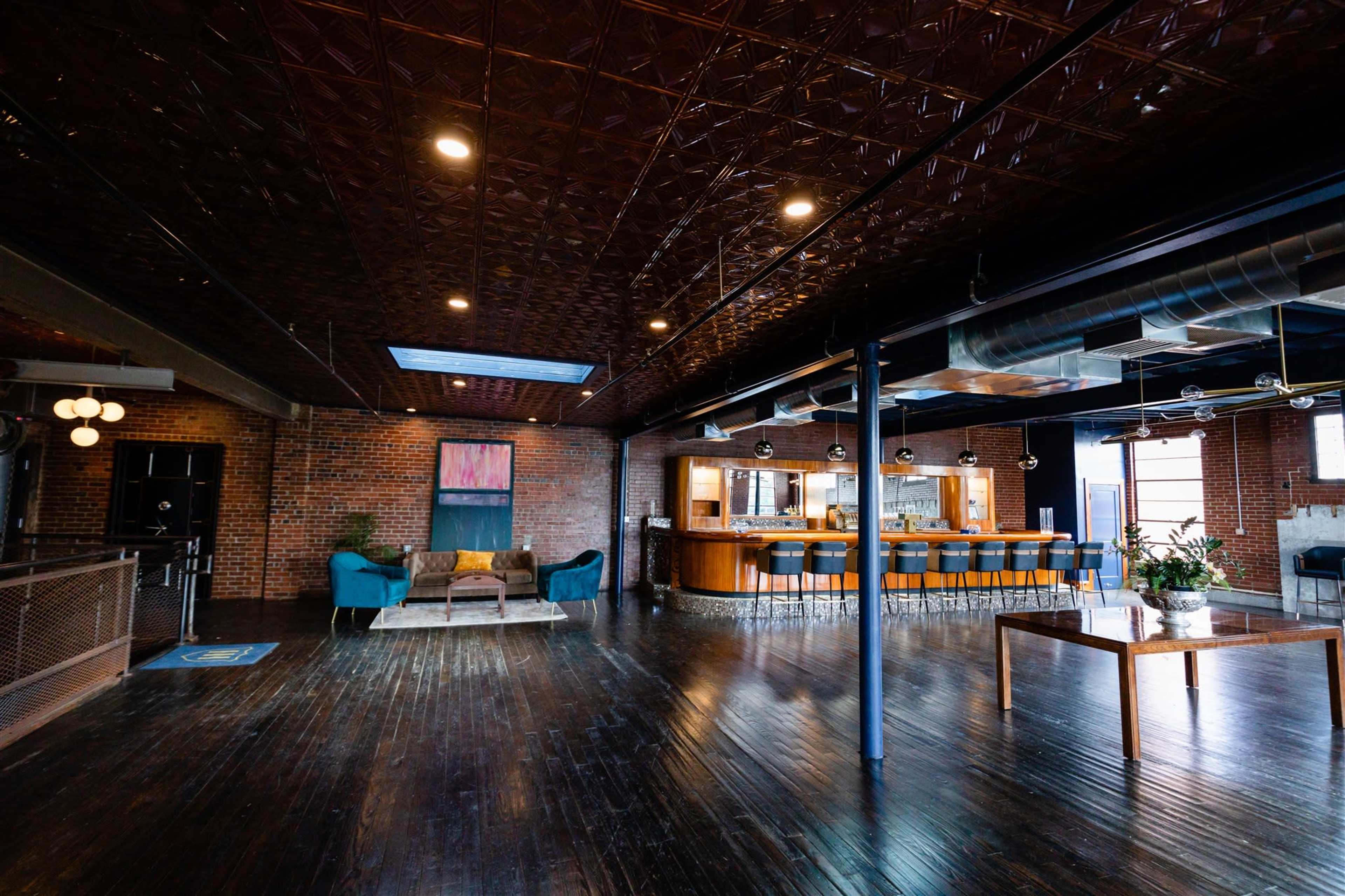A spacious rustic interior with exposed brick walls, wooden floors, and a bar area with high stools.