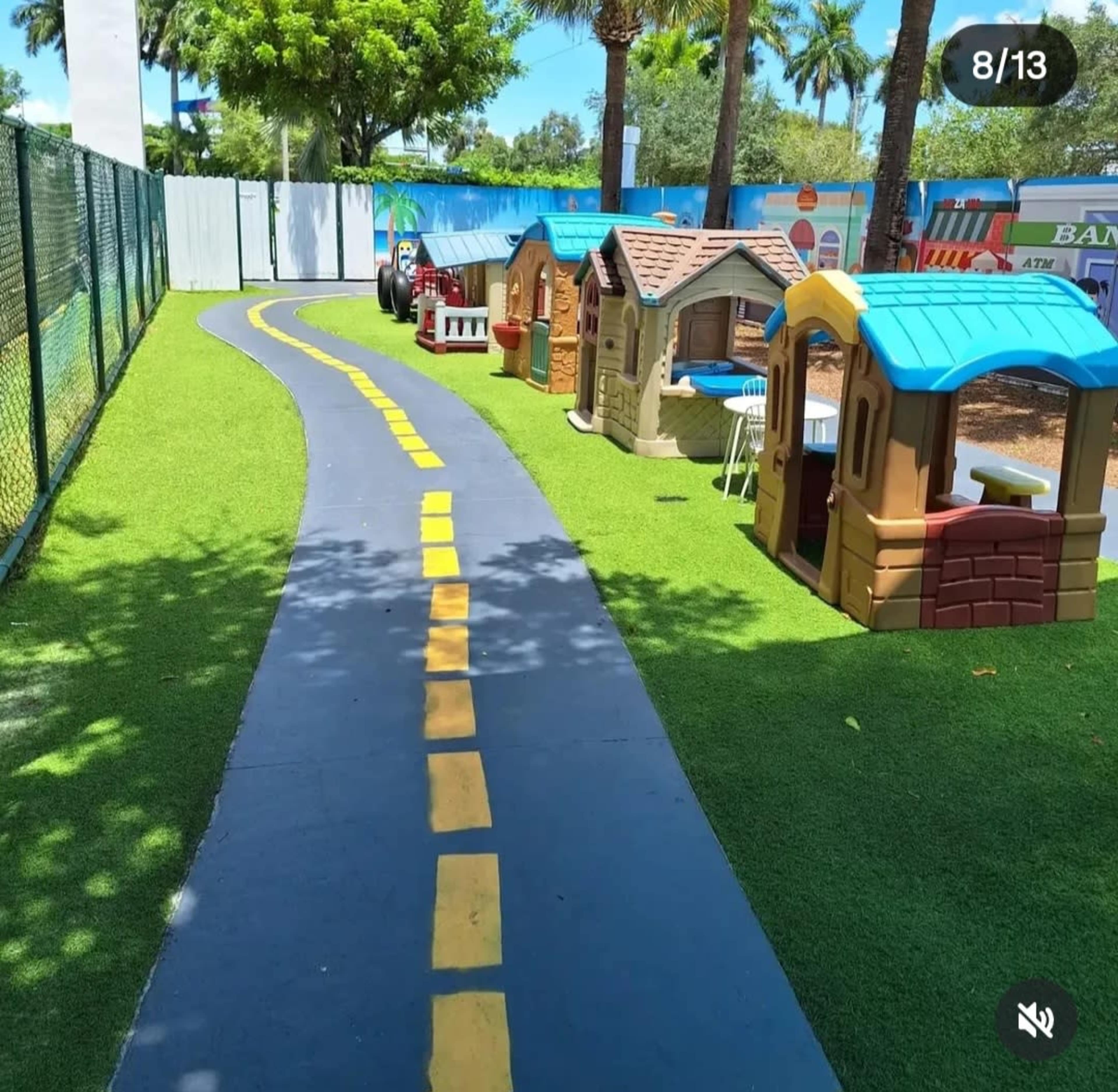 A paved path lined with yellow markers leads through a grassy area with small playhouses on either side.