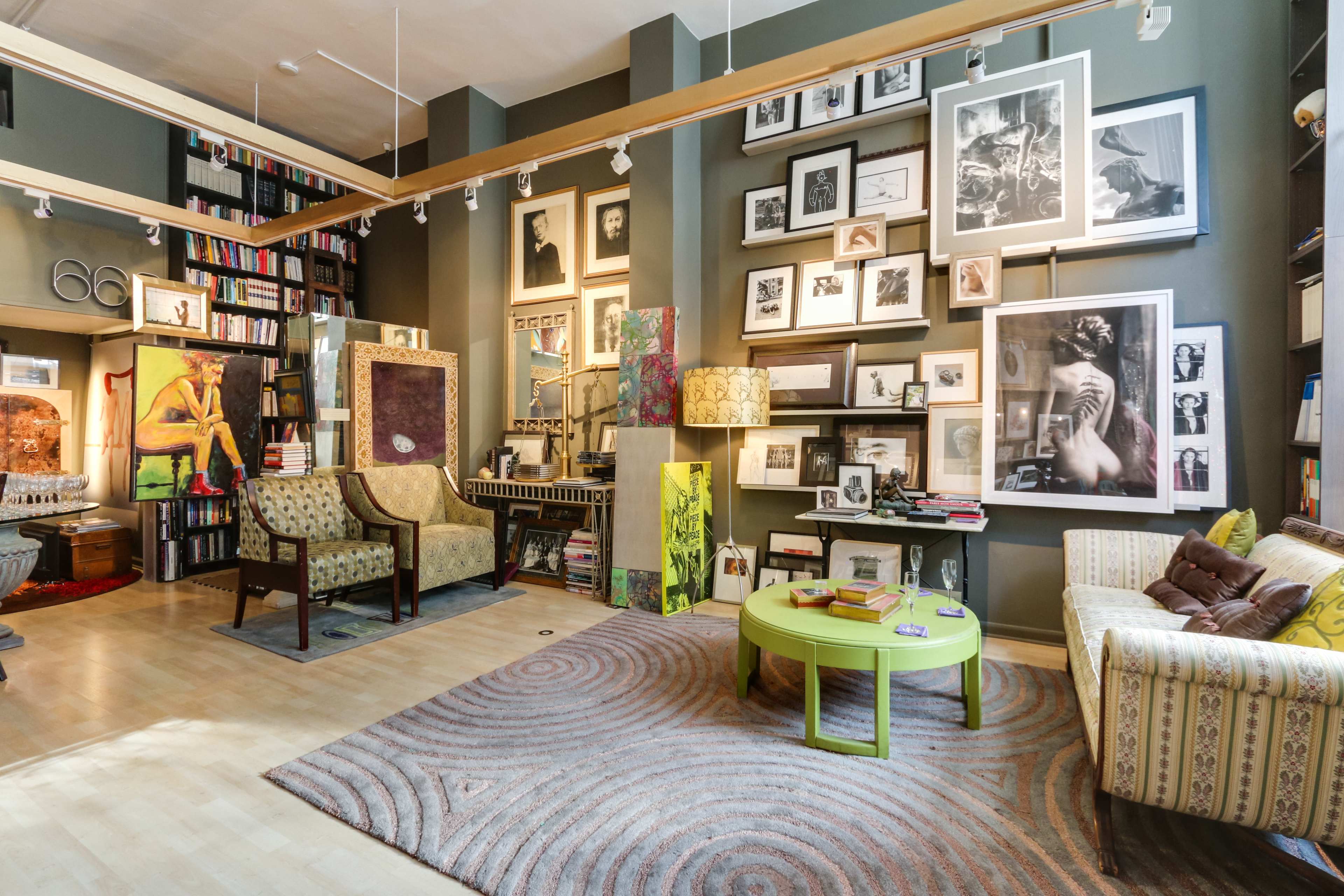 A cozy living space featuring a circular green coffee table, a patterned rug, a sofa, and walls filled with various framed artworks and bookshelves.