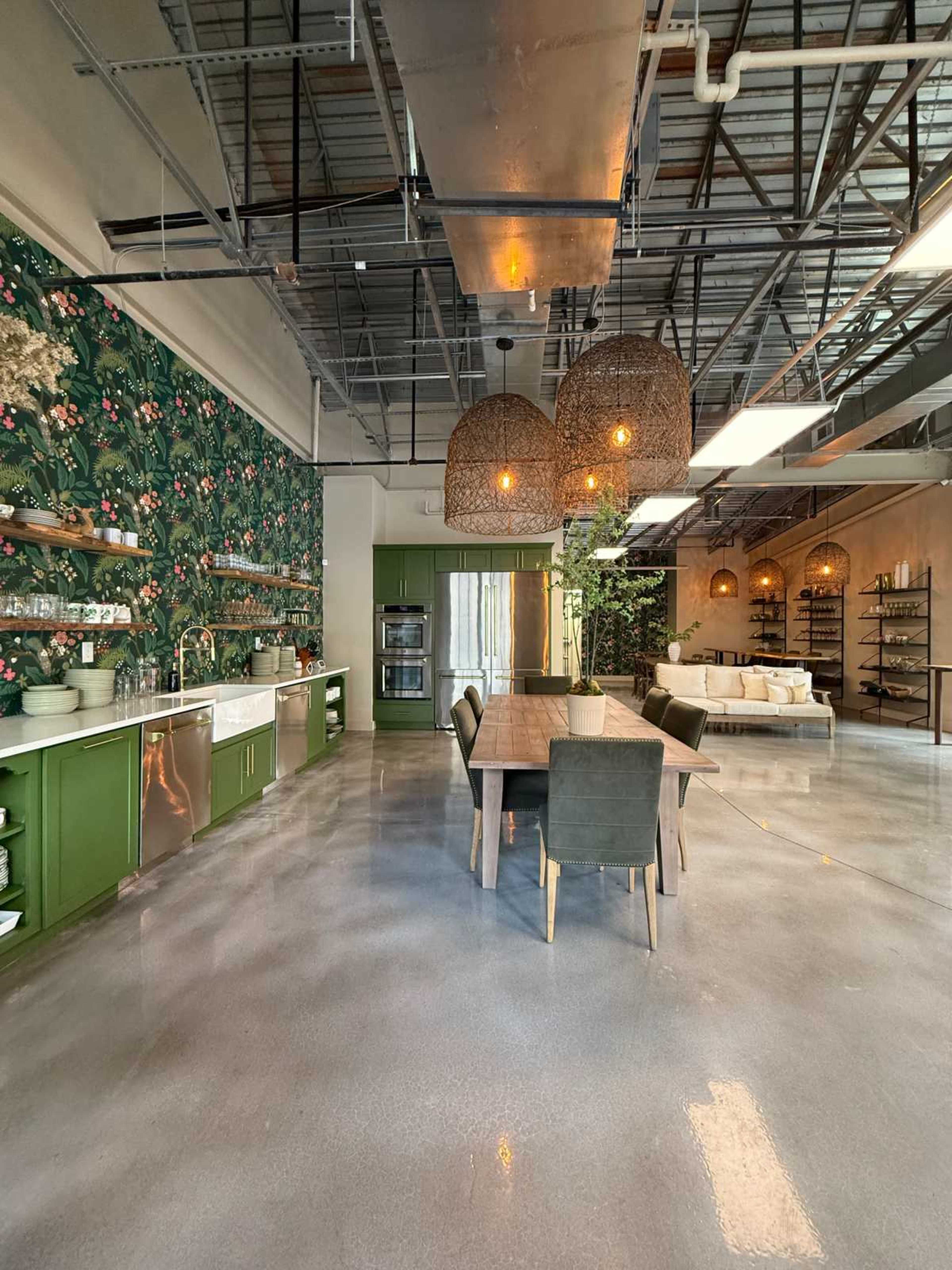 The image shows a modern kitchen and dining area featuring a green cabinetry, a wooden dining table with gray chairs, and decorative wall plants.