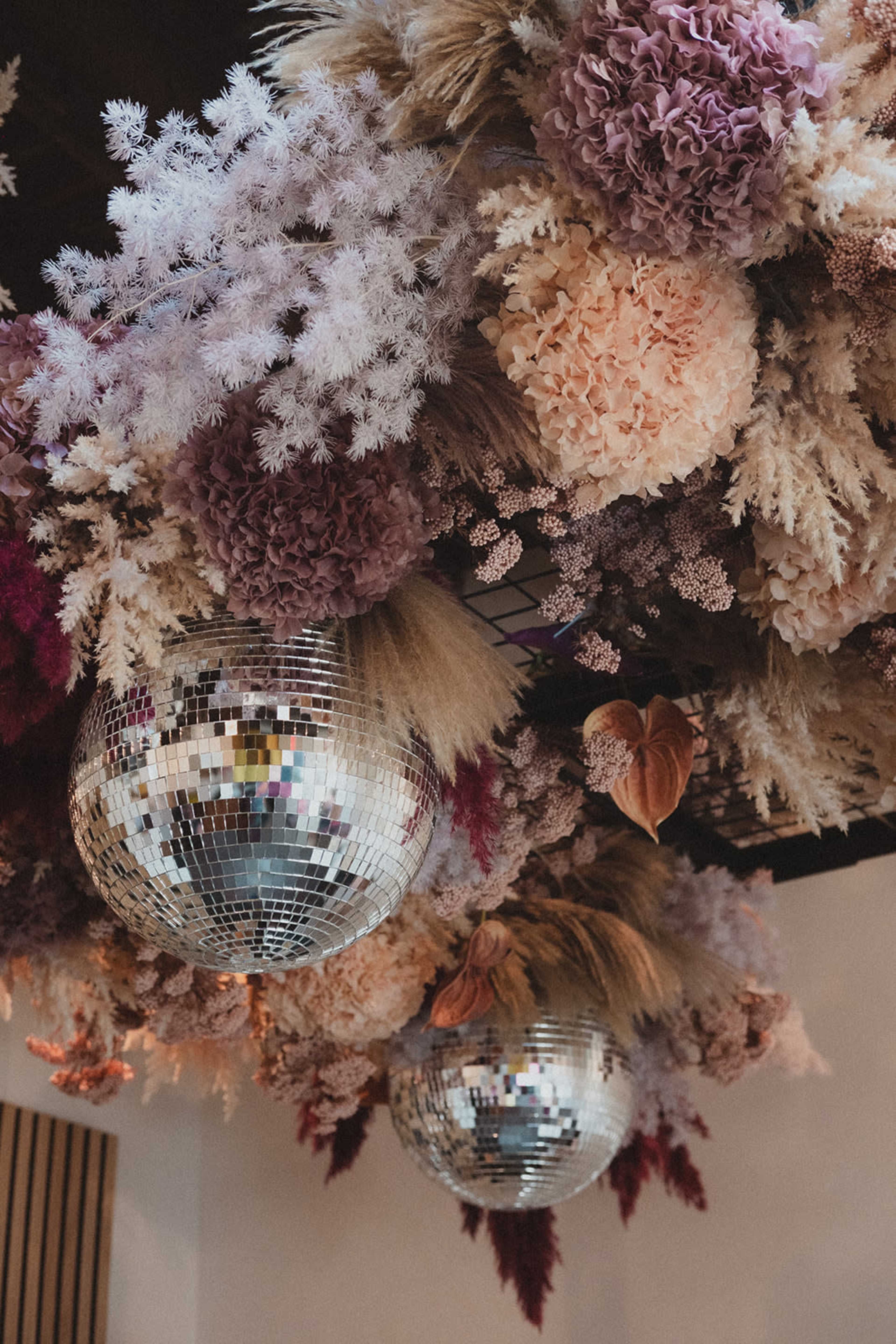 The image shows a ceiling decorated with dried flowers in various colors and two disco balls.