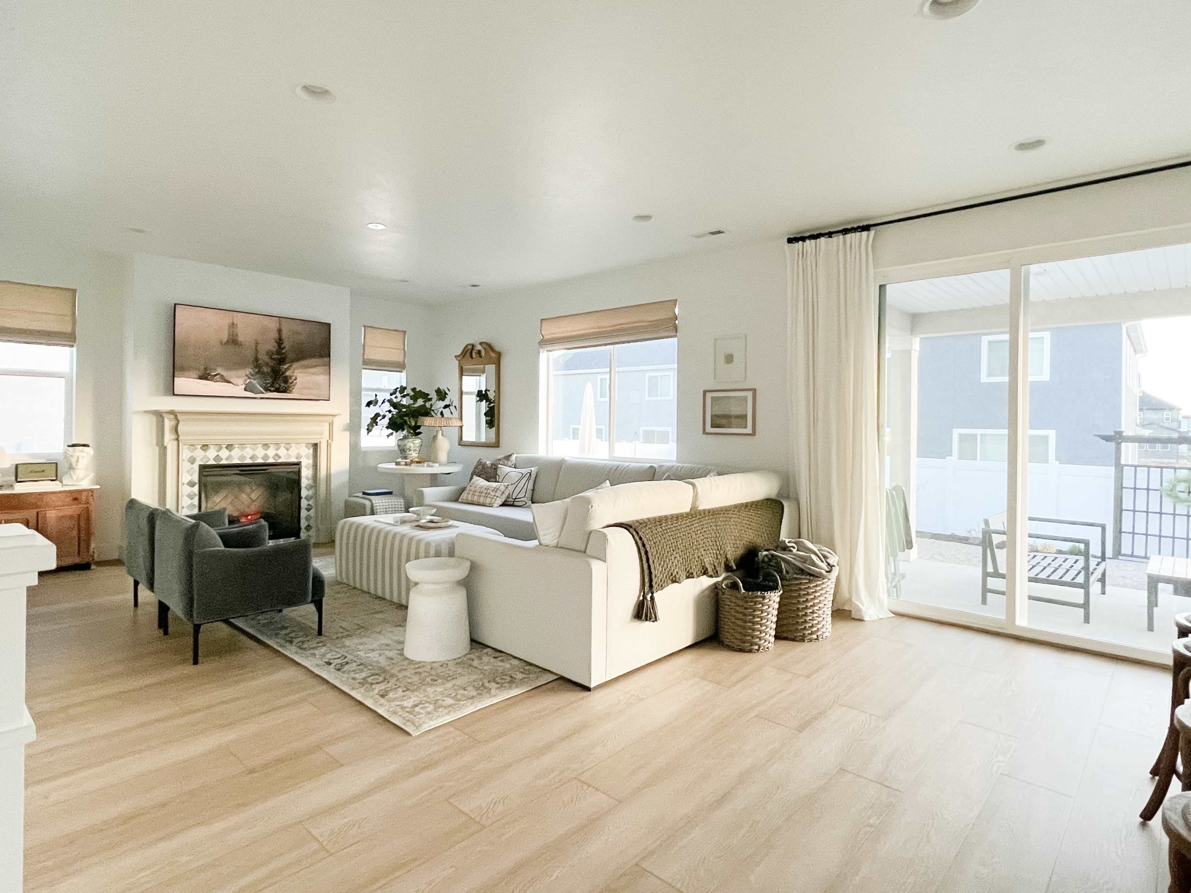 The image shows a modern living room with a white sofa, a fireplace, and a sliding glass door leading to an outdoor patio.