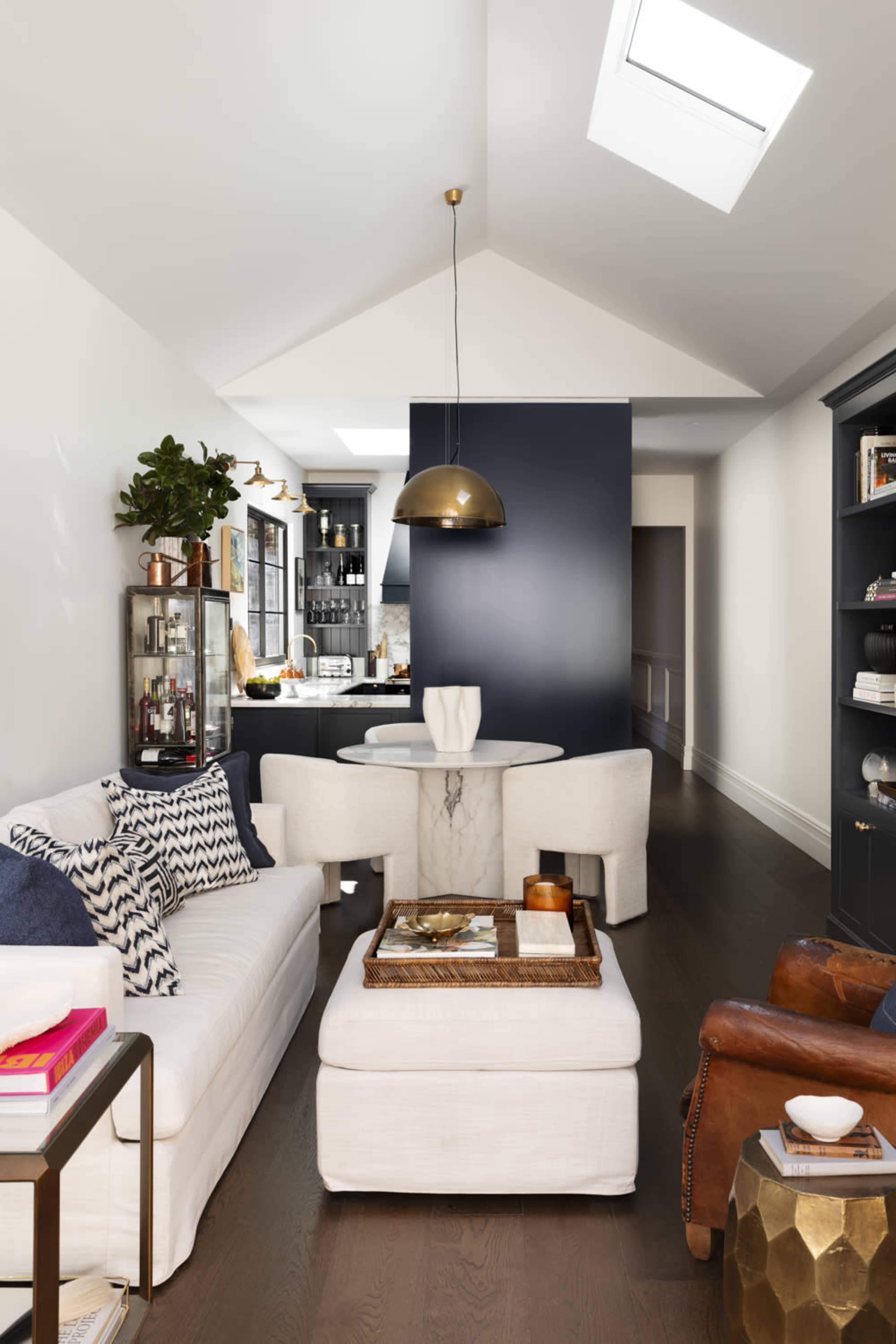 A modern living space featuring a white sofa, a round white table, and a dark blue accent wall, with a tray on an ottoman and a bookshelf in the background.