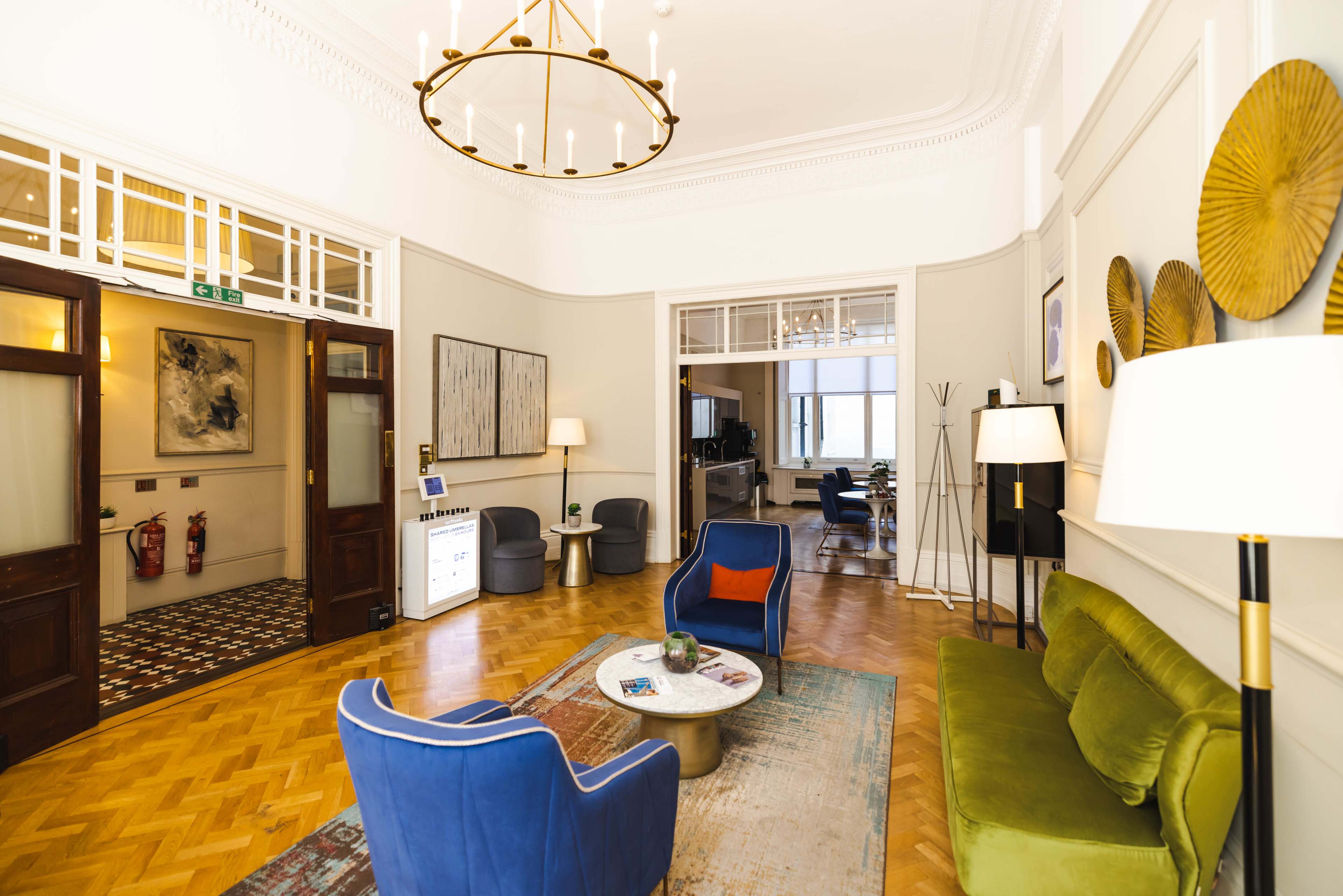 A spacious lobby area with a green sofa, blue armchairs, a circular coffee table, and decorative wall elements.
