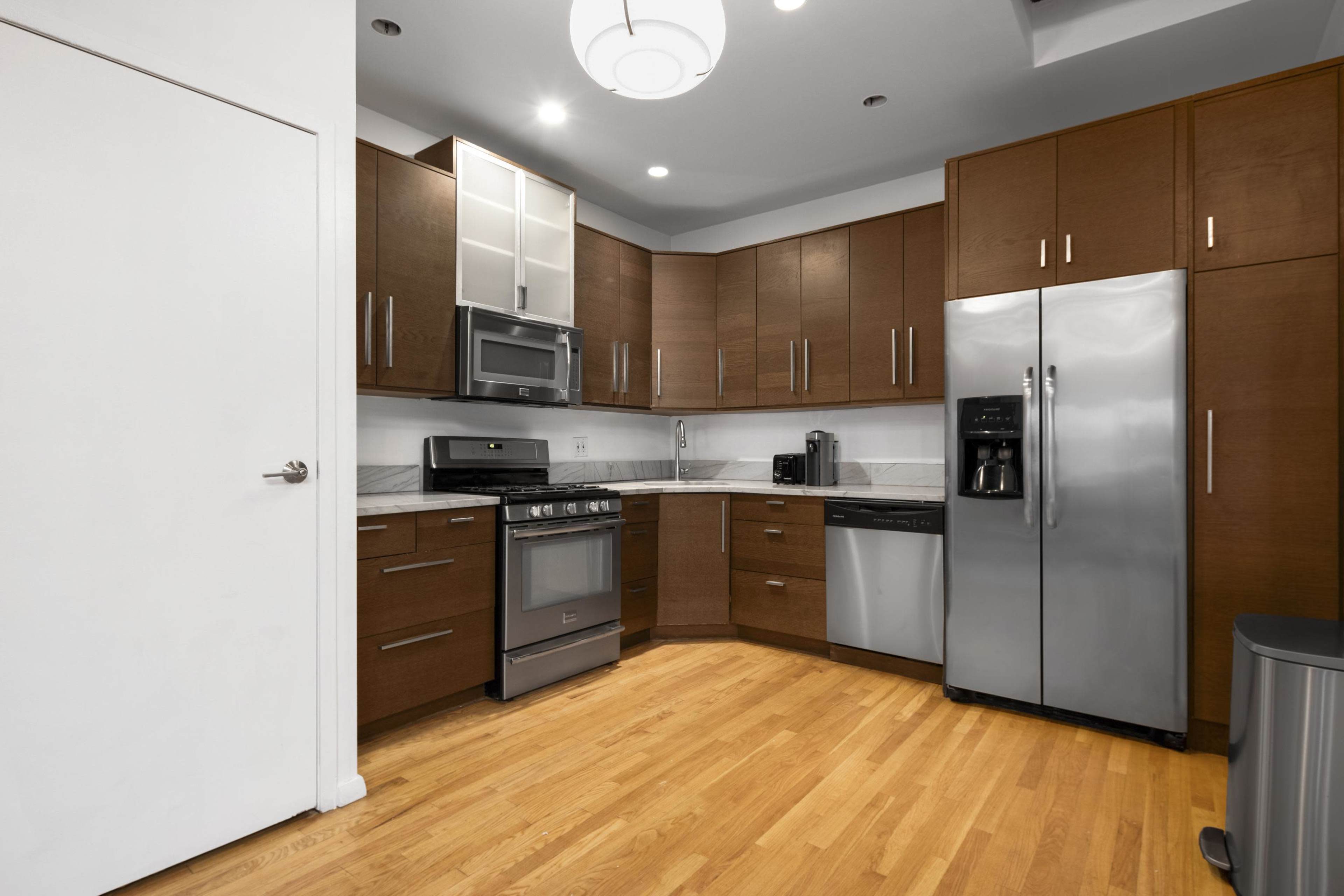A modern kitchen with wooden cabinets, stainless steel appliances, and a hardwood floor.