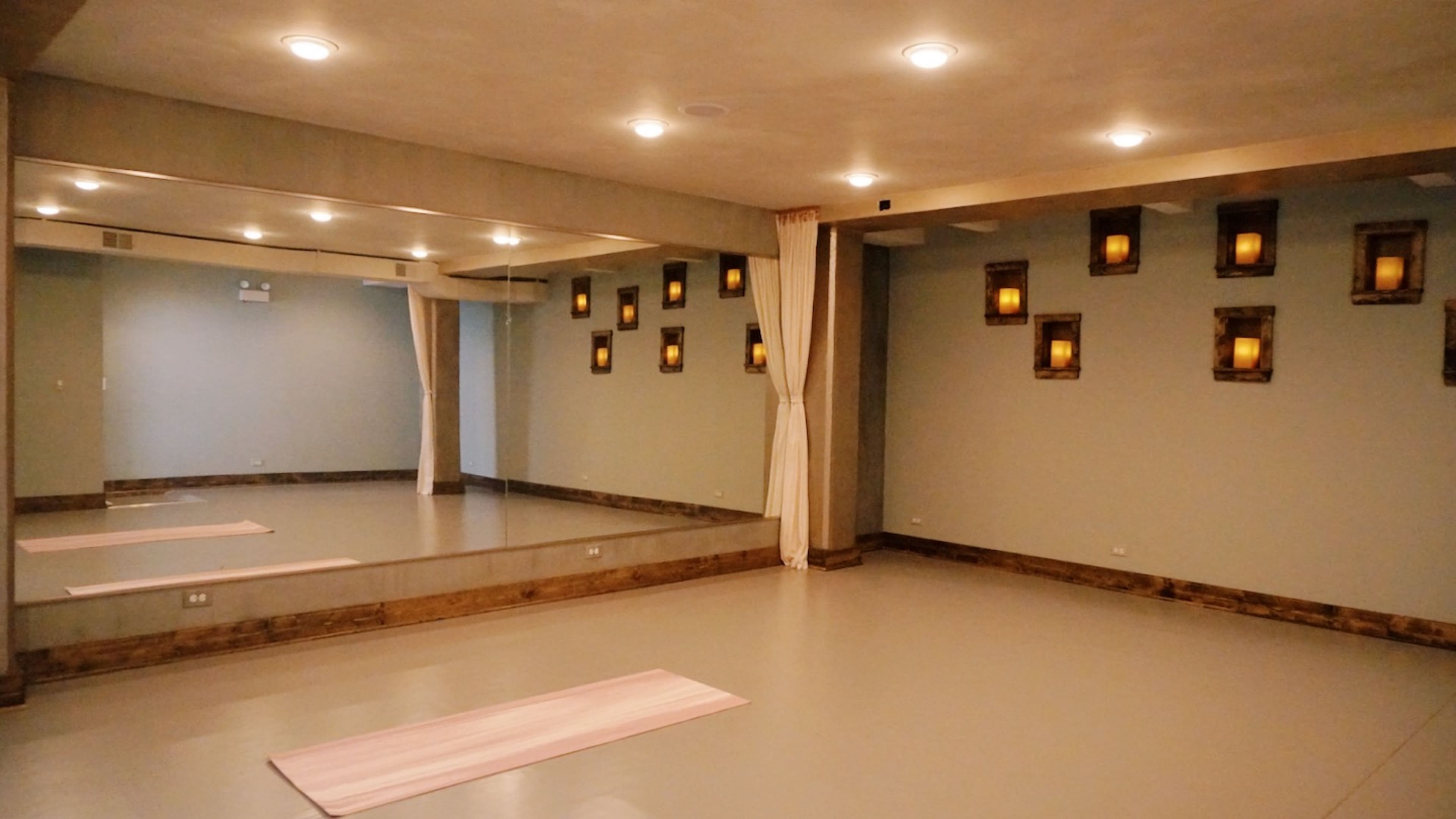 A yoga studio with mirrored walls, wooden accents, and softly lit wall sconces.