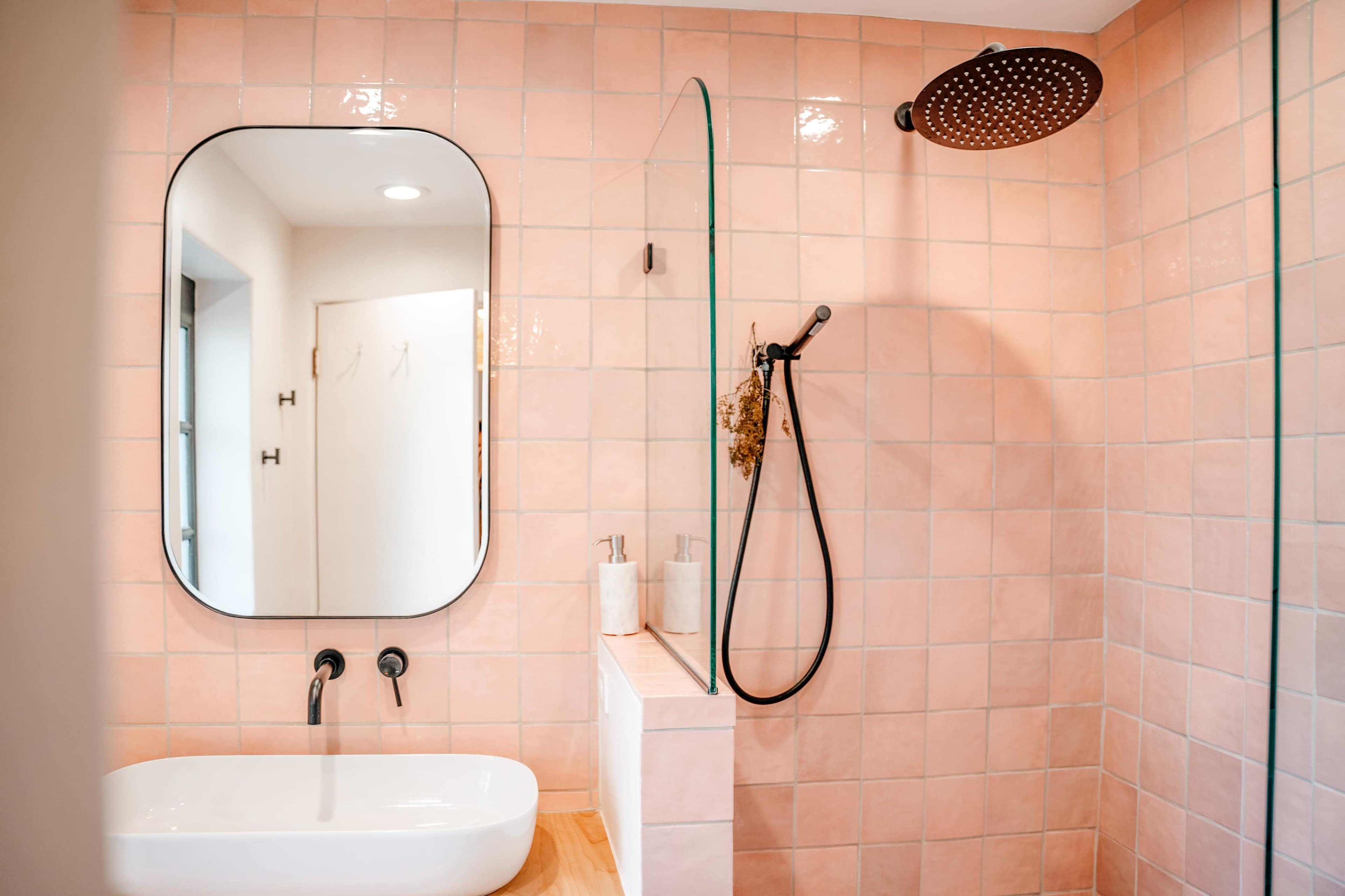 A bathroom features pink tiled walls, a freestanding white bathtub, and a glass shower enclosure with a overhead rainfall showerhead.