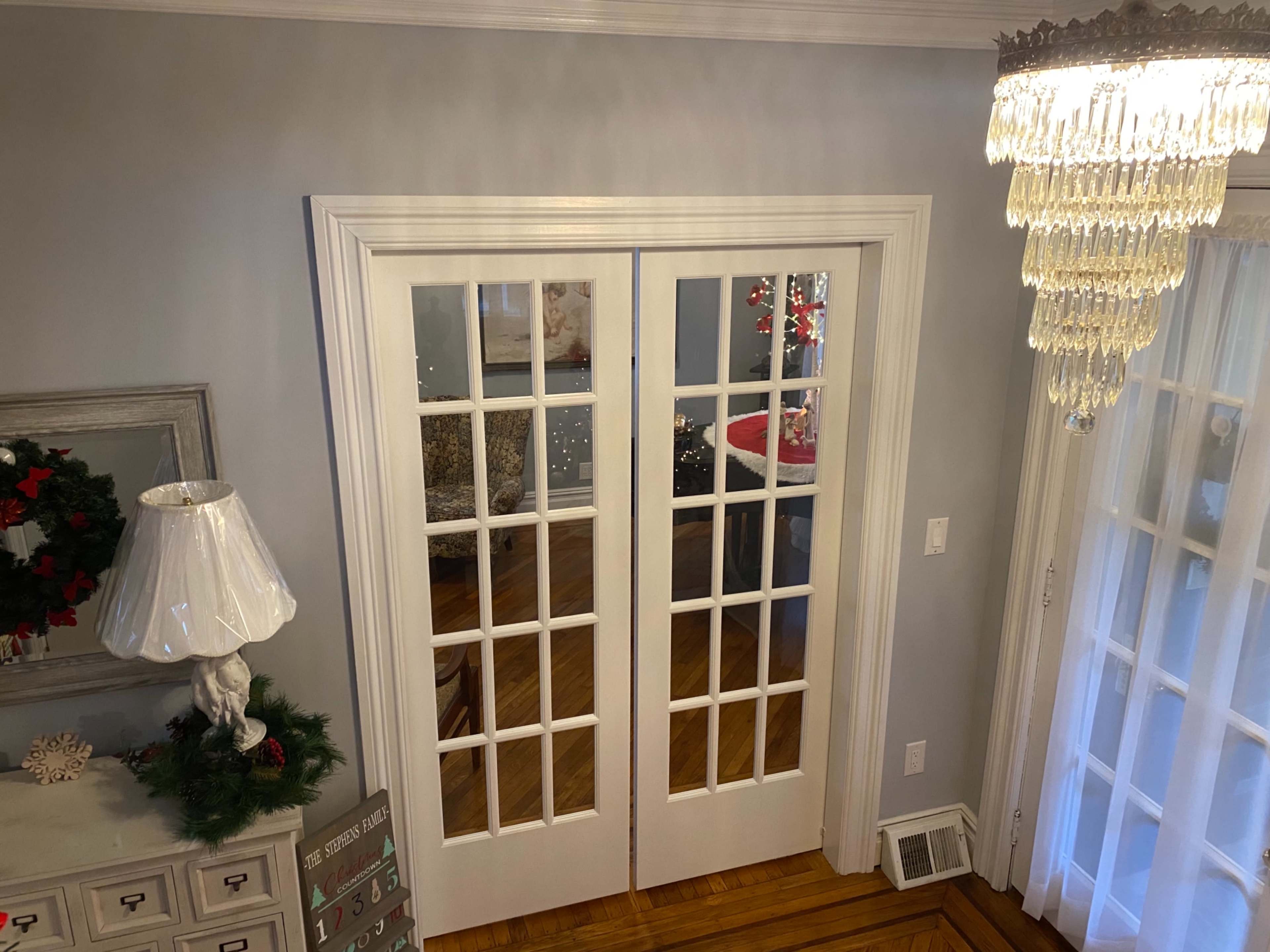 A set of double French doors with glass panels, located in a well-lit room featuring a chandelier and holiday decorations.