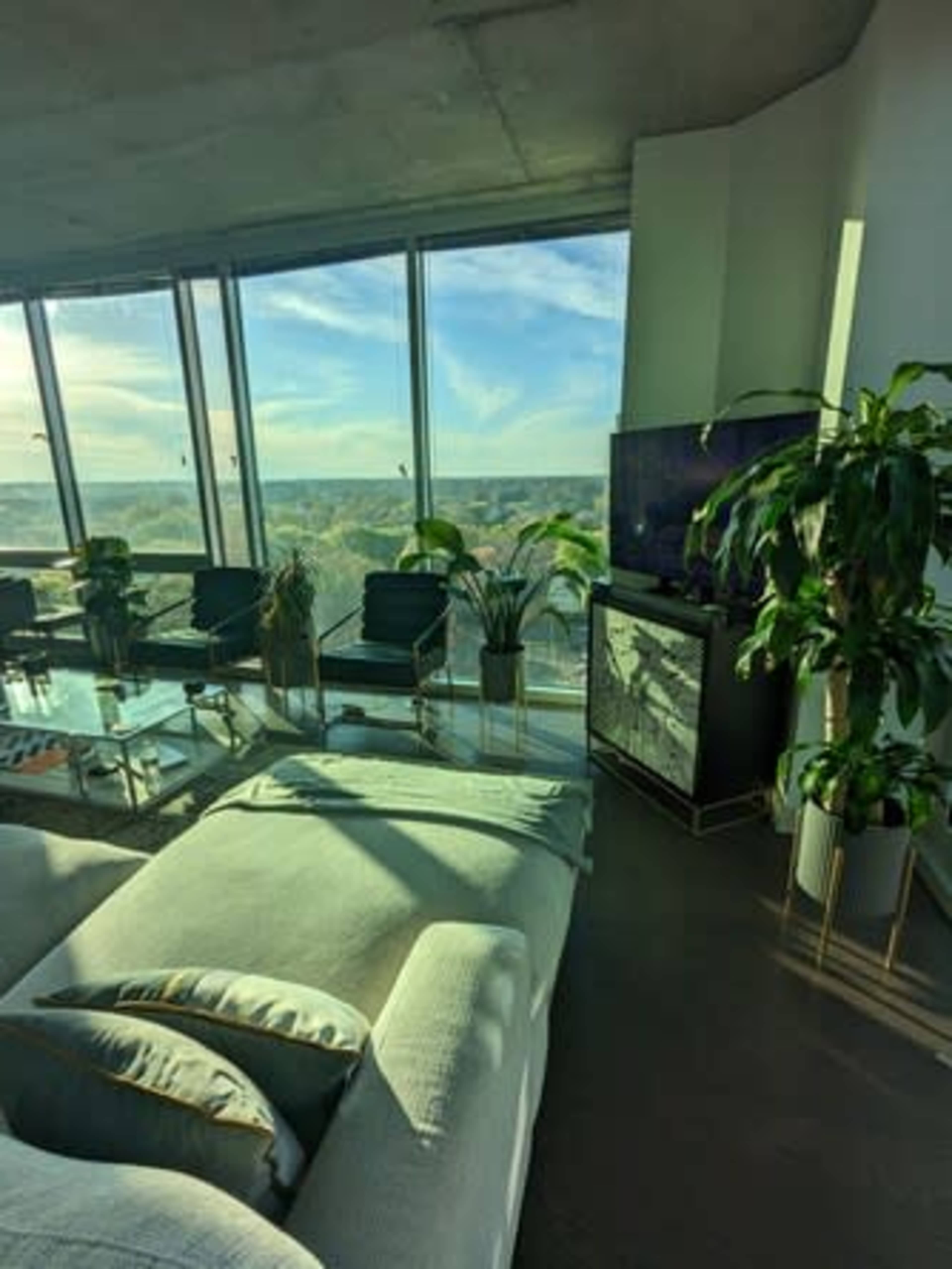 A modern living room features a comfortable sofa, glass furniture, and large windows that offer a view of the landscape outside.