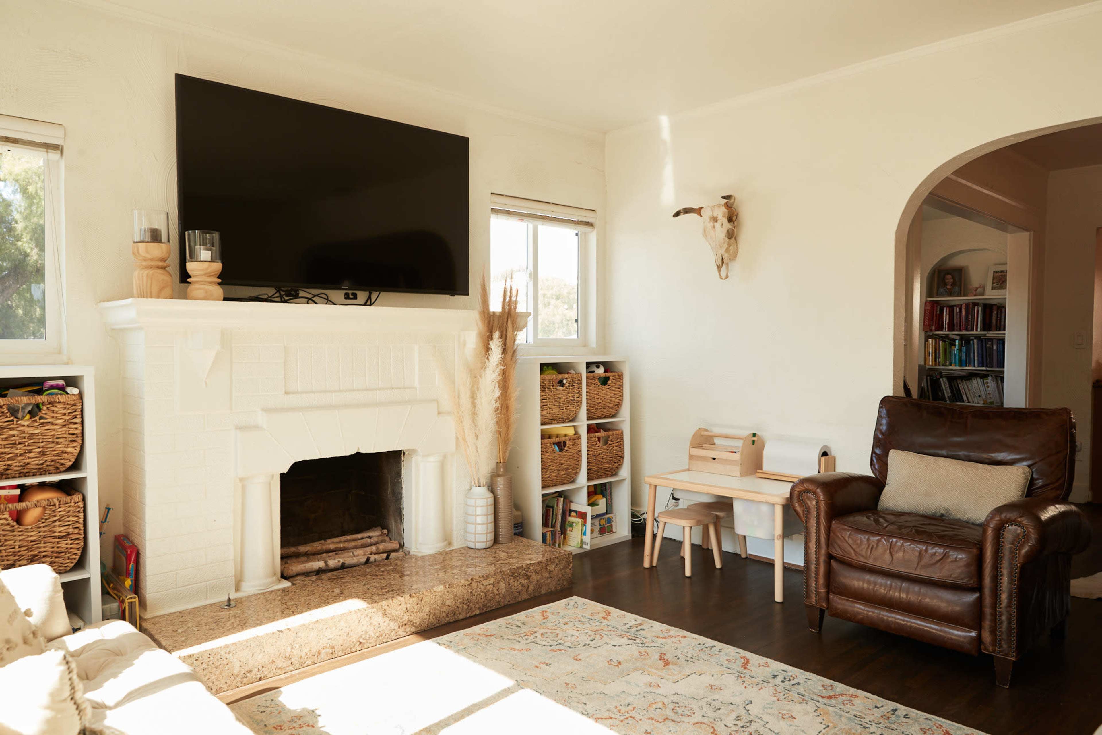 The living room features a large television mounted above a white brick fireplace, with comfortable seating and organized storage baskets.
