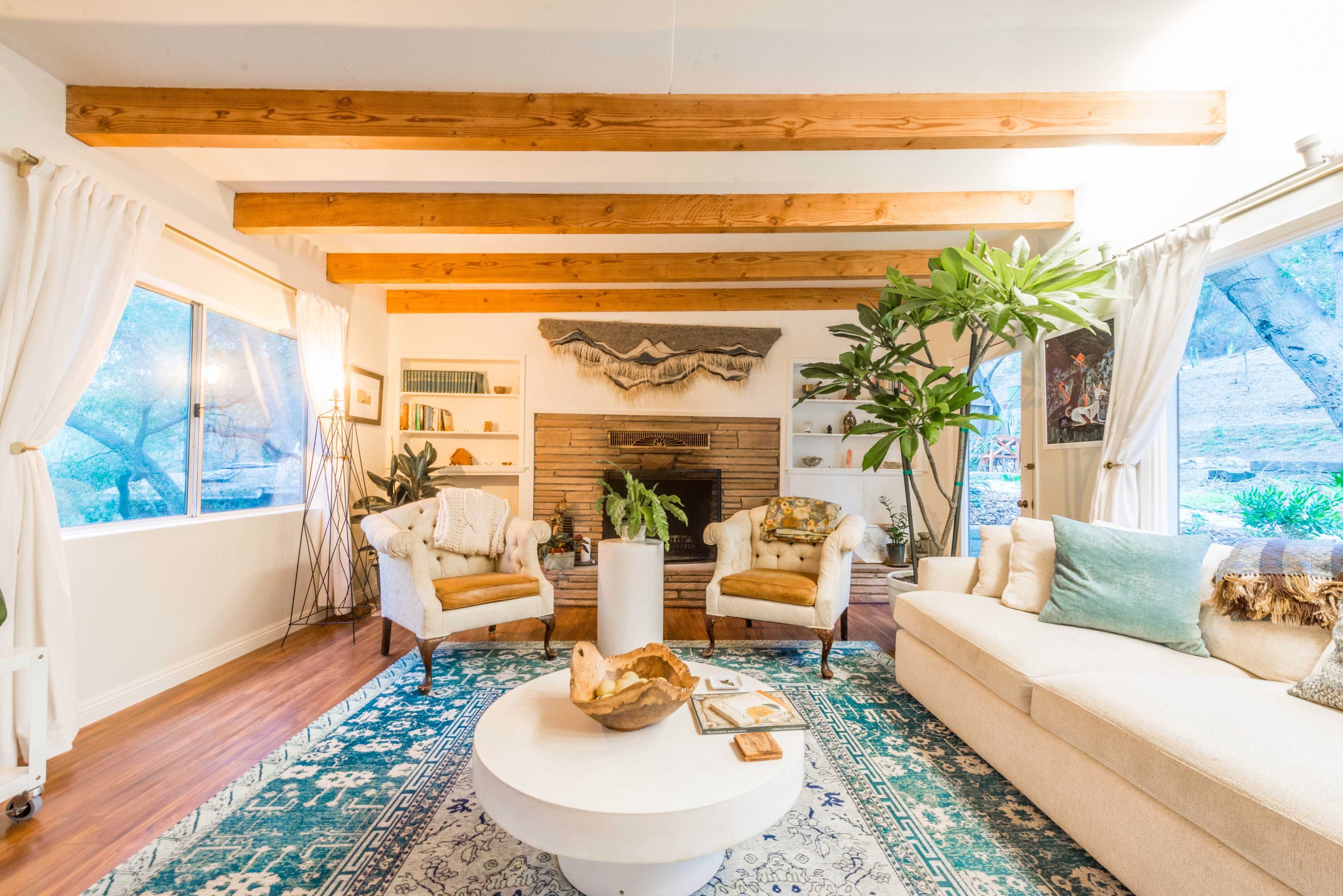 The living room features two armchairs, a sectional sofa, a coffee table, and a fireplace, accented by wooden beams and large windows.