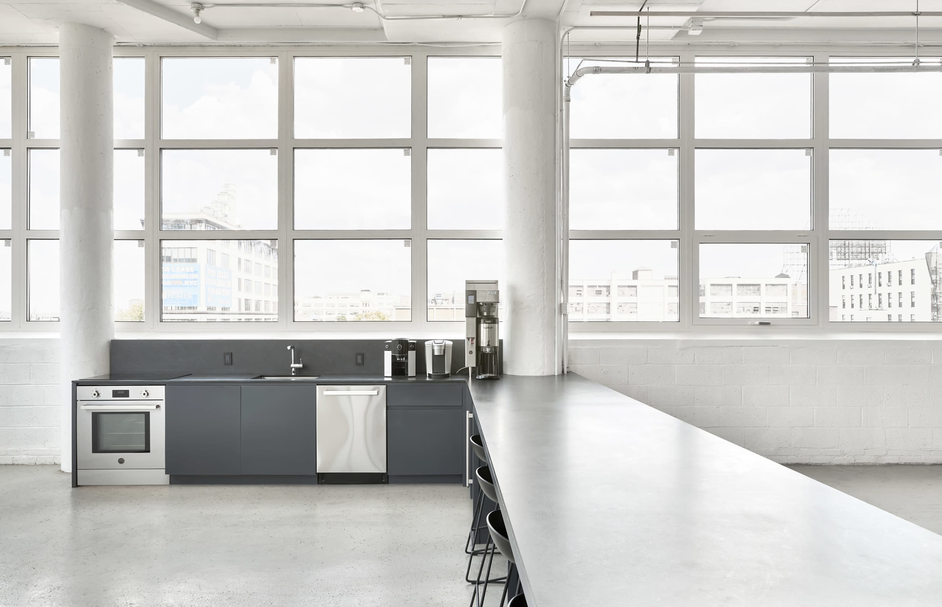 A modern kitchen features grey cabinetry, stainless steel appliances, and large windows that provide ample natural light.