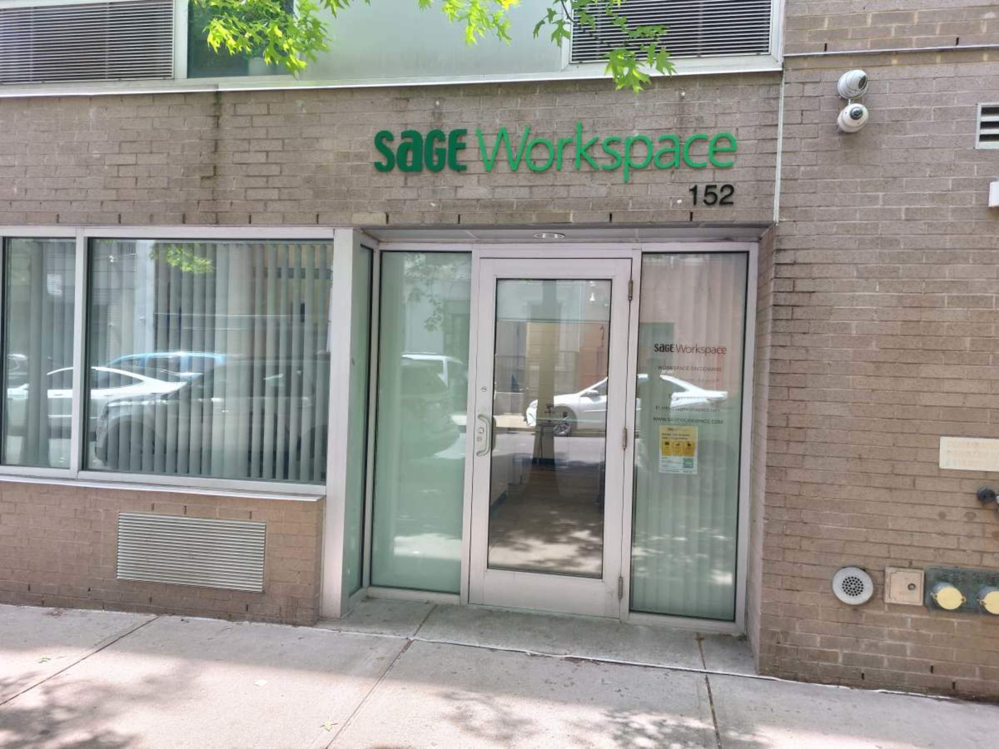 The image shows the entrance of a building labeled "Sage Workspace" at the address 152, featuring glass doors and a brick exterior.