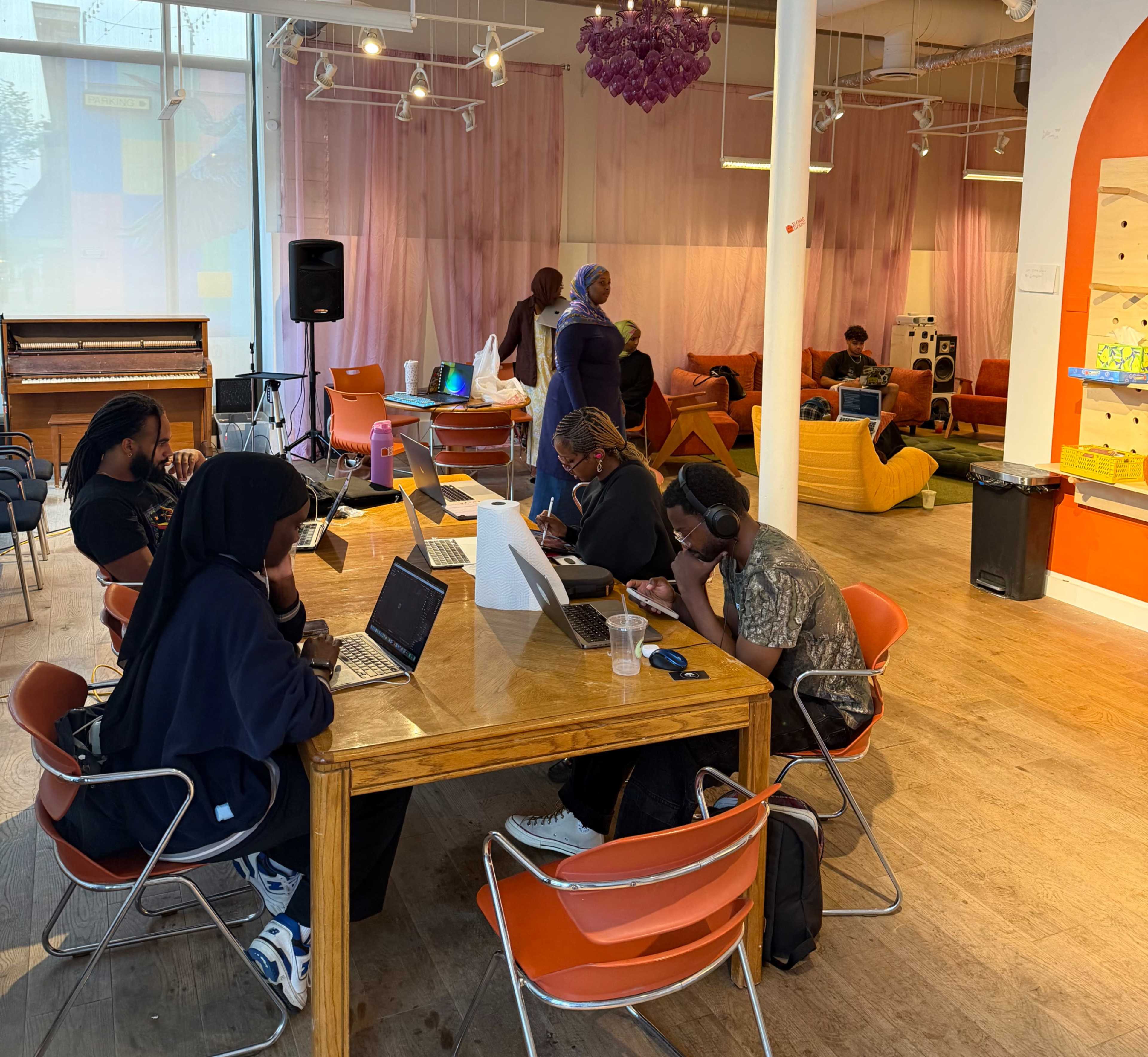 A group of people is working at a table with laptops in a colorful, open, and modern co-working space.
