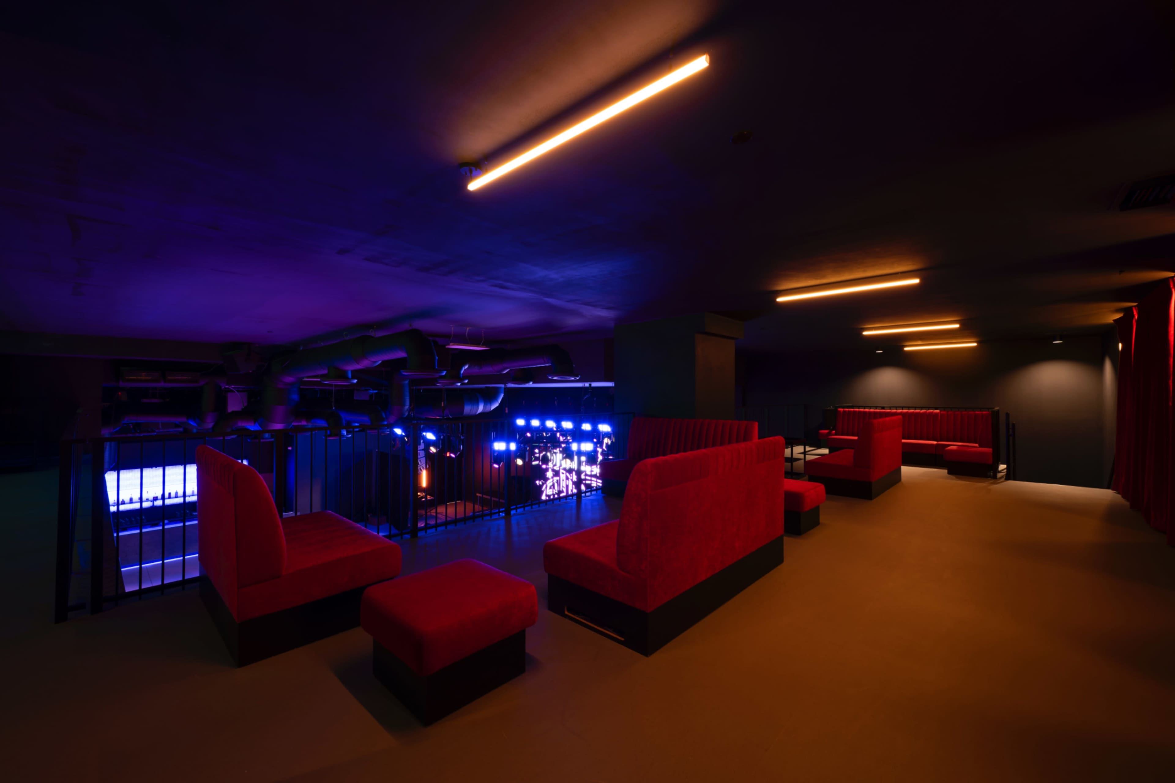 The image shows a dimly lit lounge area featuring red seating and blue lighting in the background that suggests a performance space.