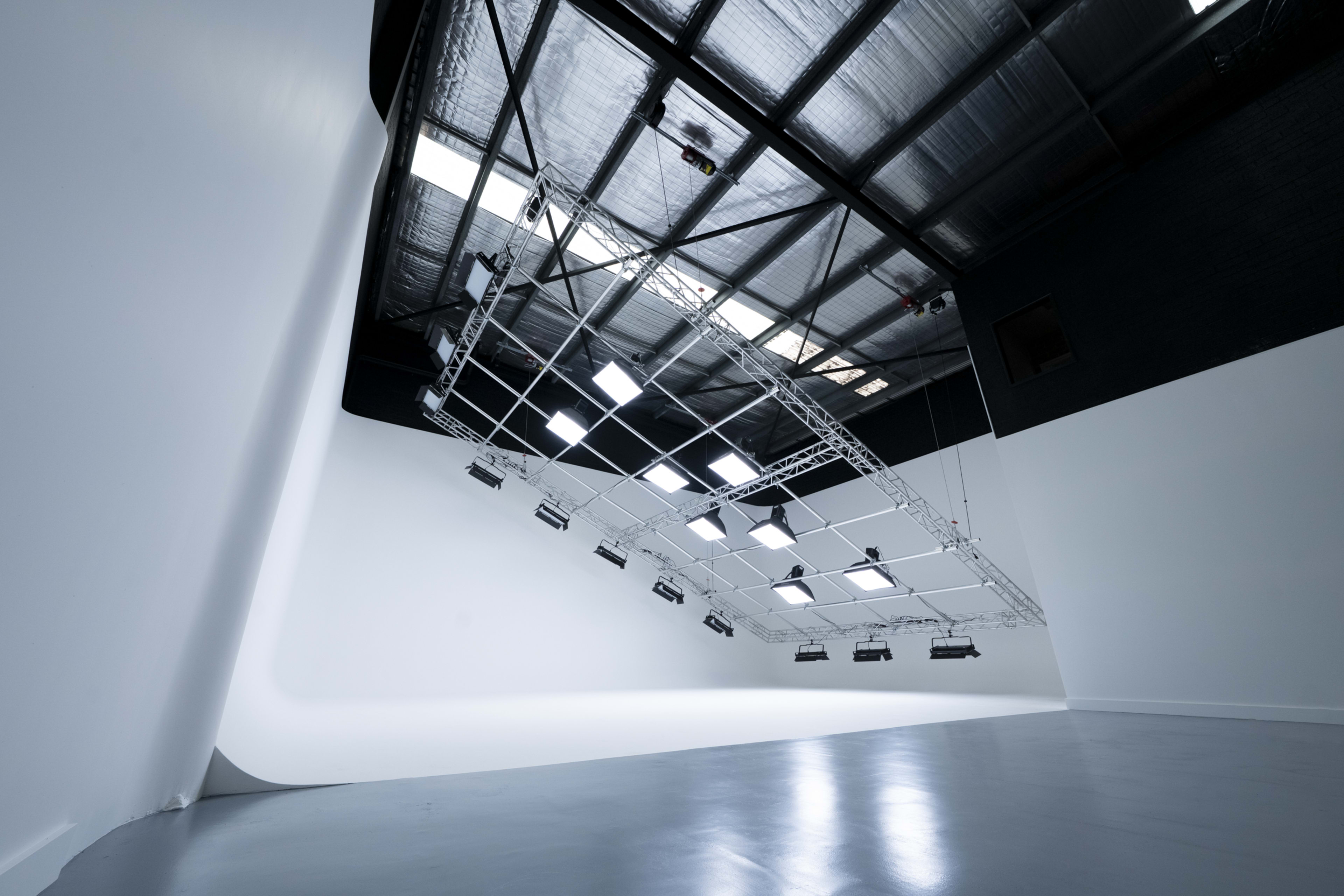 The image shows a spacious photography studio with a tilted ceiling and multiple lights suspended from a metal frame.