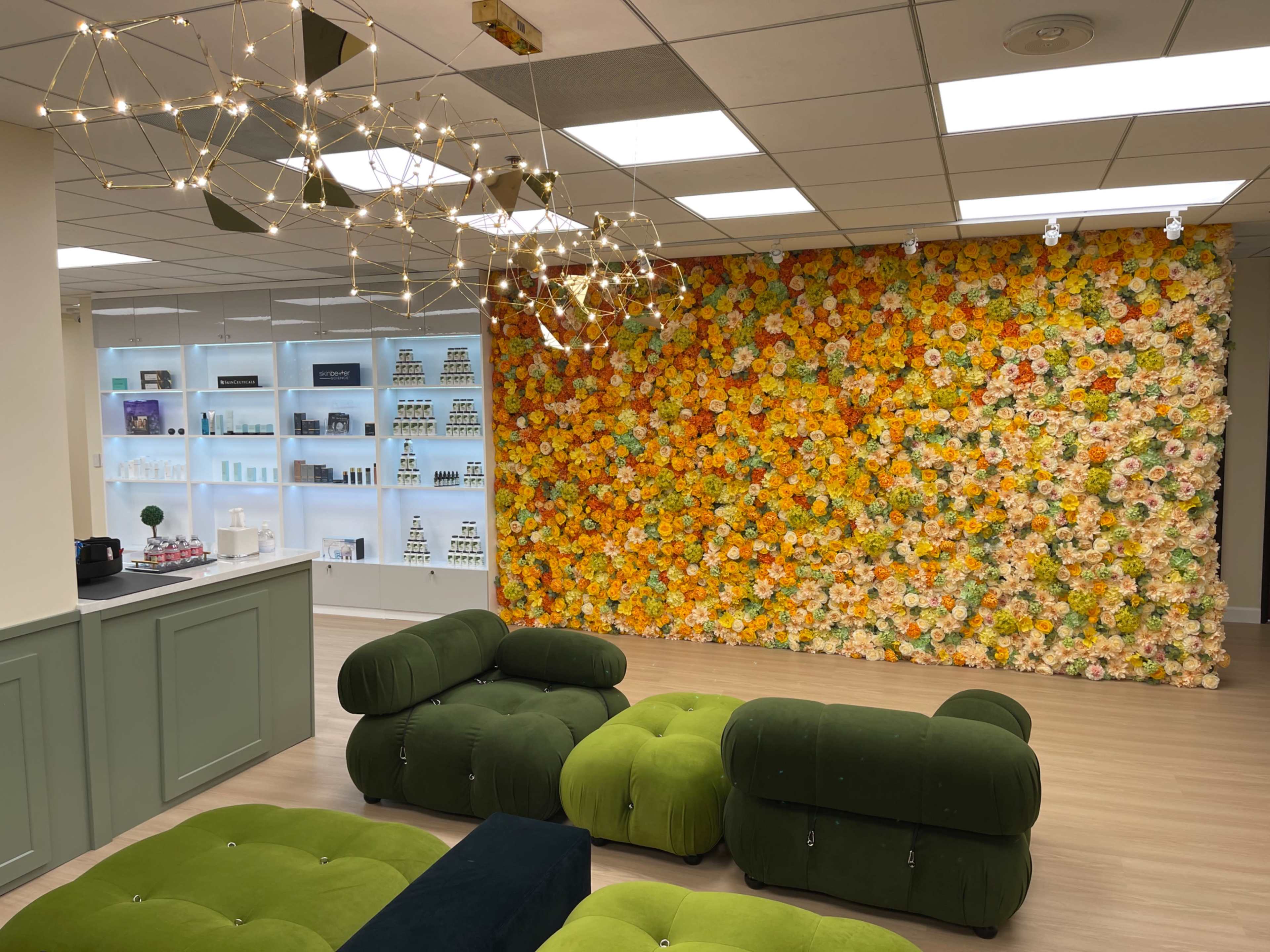 A modern room with a vibrant floral wall, stylish green tufted seating, and shelves displaying various products.