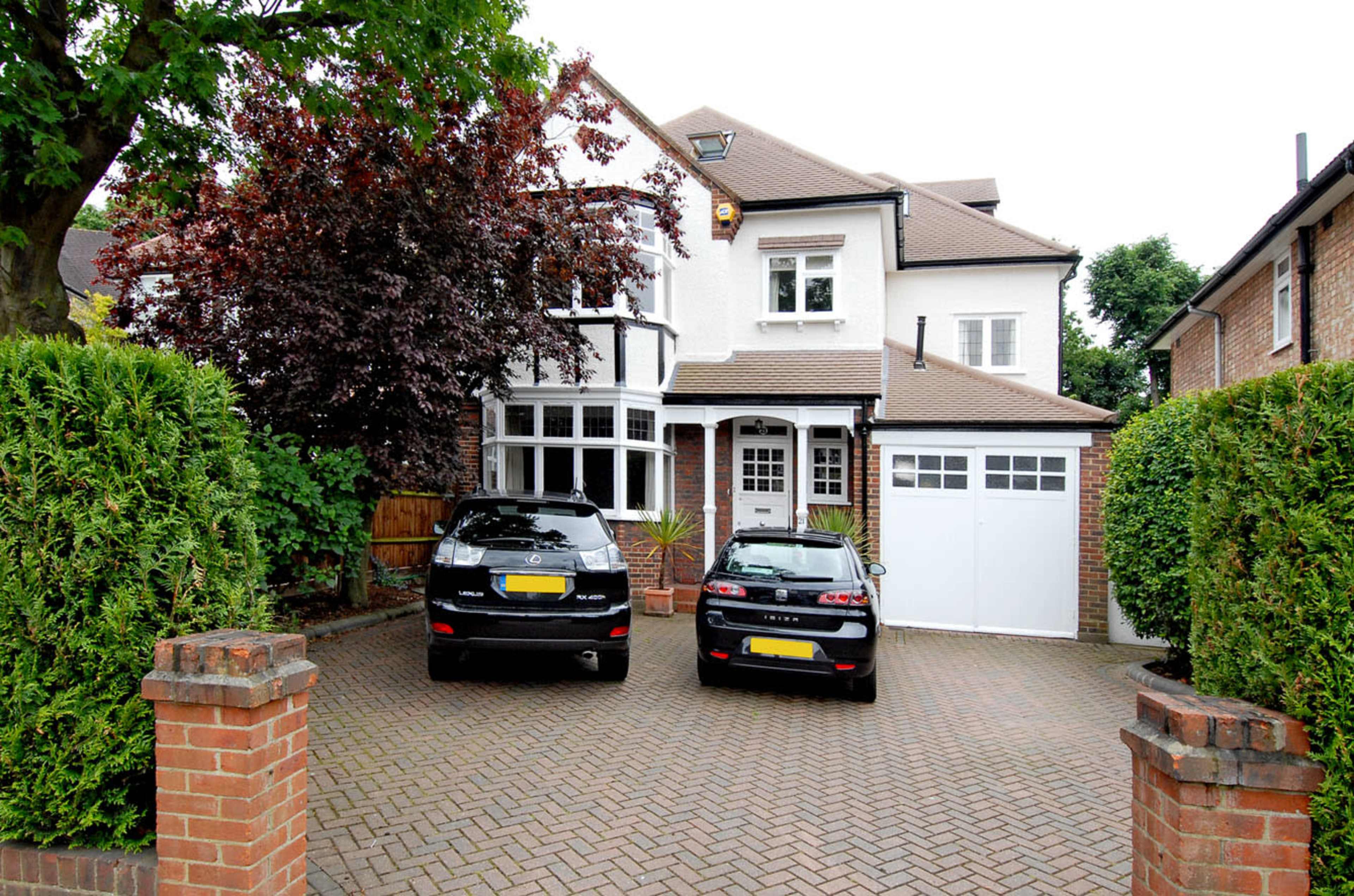 A two-story house with a front garden and two parked black cars in the driveway.