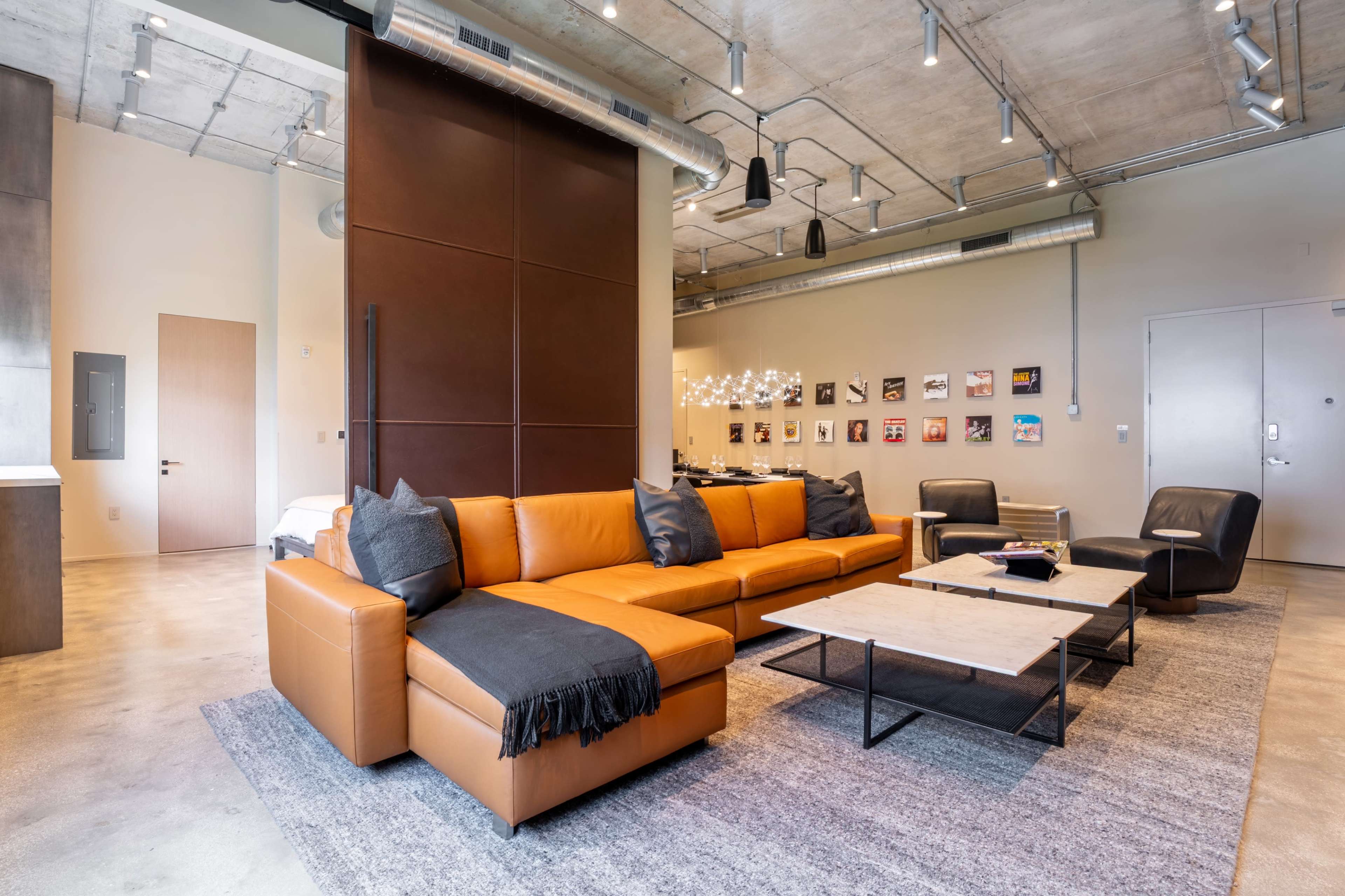 The image shows a modern living room with a large orange sectional sofa, a coffee table, and several framed pictures on the wall.