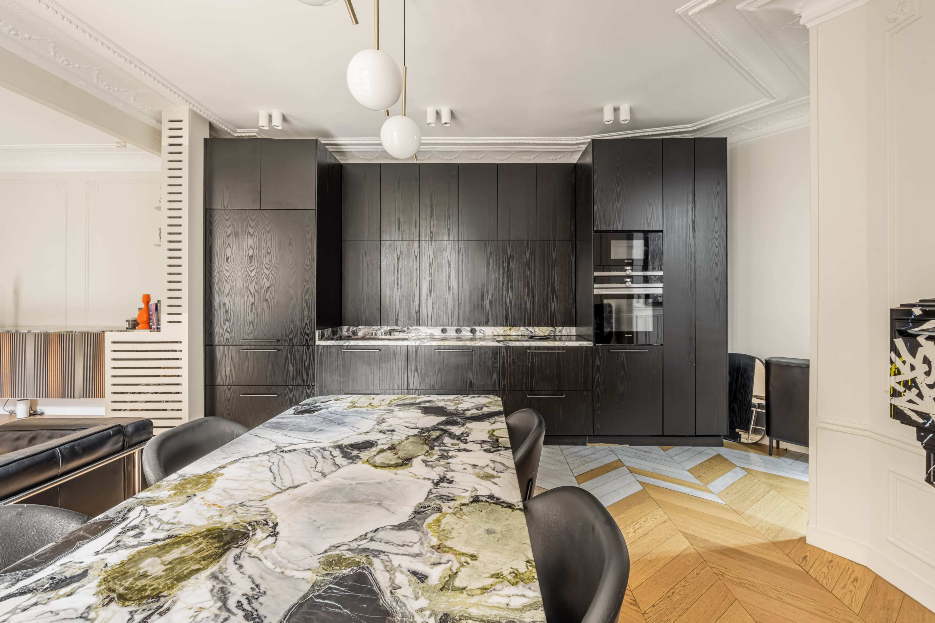 A modern kitchen features black cabinetry, a marble table with green and white patterns, and a mix of hardwood and patterned flooring.