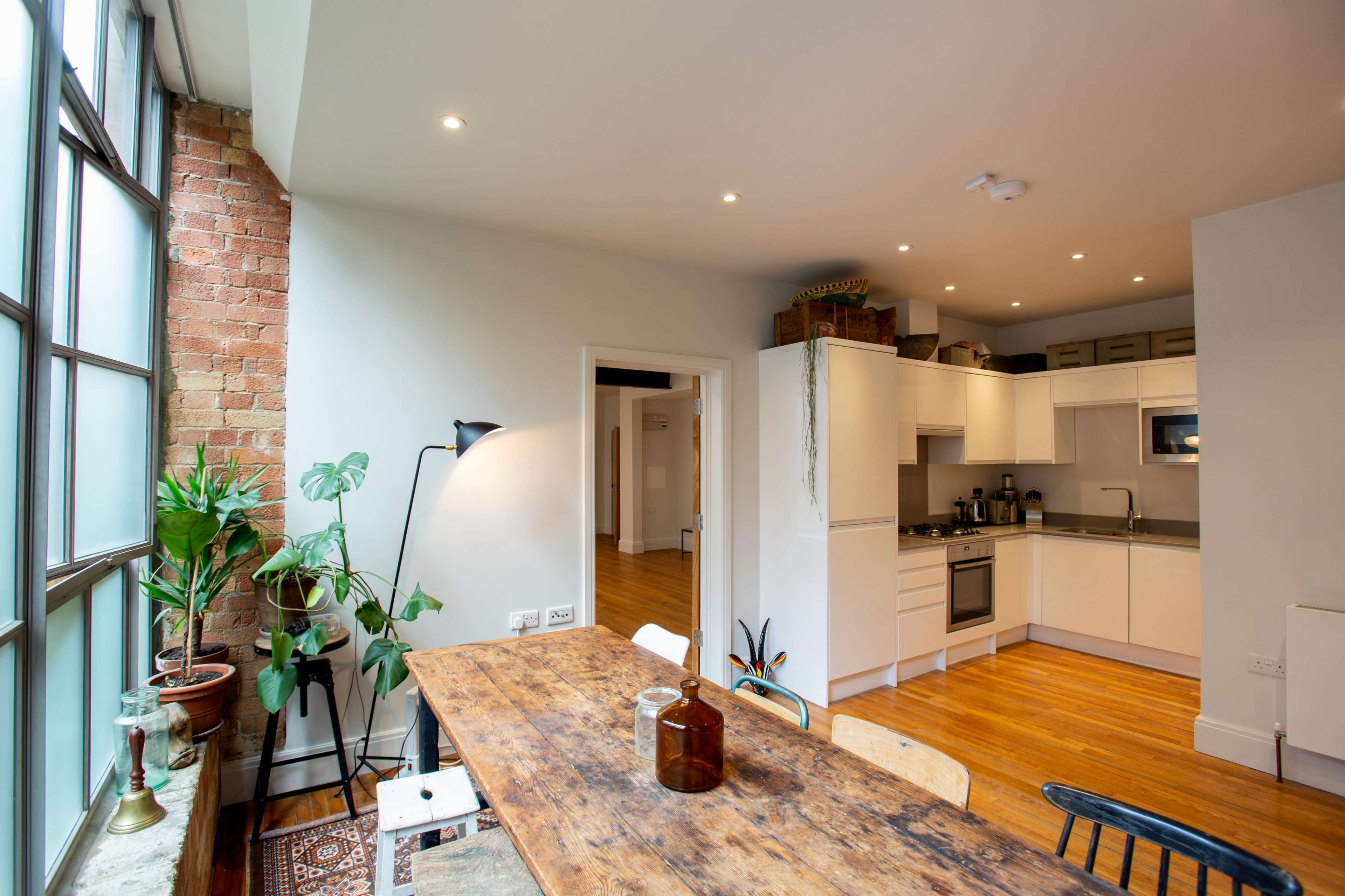 A modern kitchen and dining area with wooden flooring, a large window, and a rustic dining table surrounded by chairs.